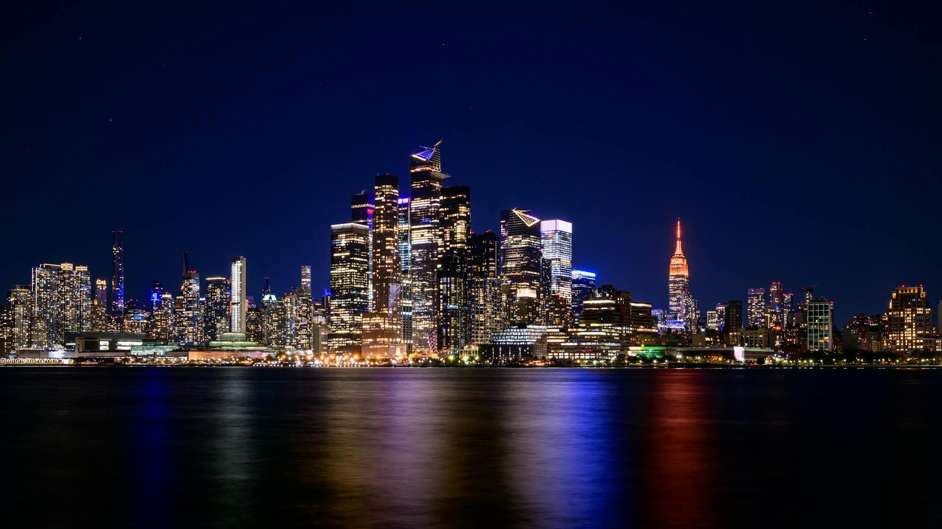 Breathtaking view of New York City skyline with vibrant city lights reflecting on water at night.
