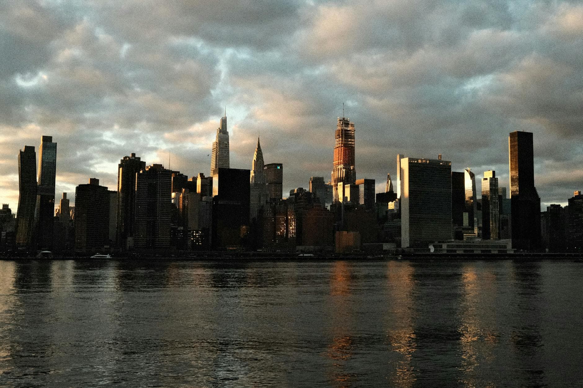 Dramatic view of Manhattan skyline during twilight with city reflection on water, New York.
