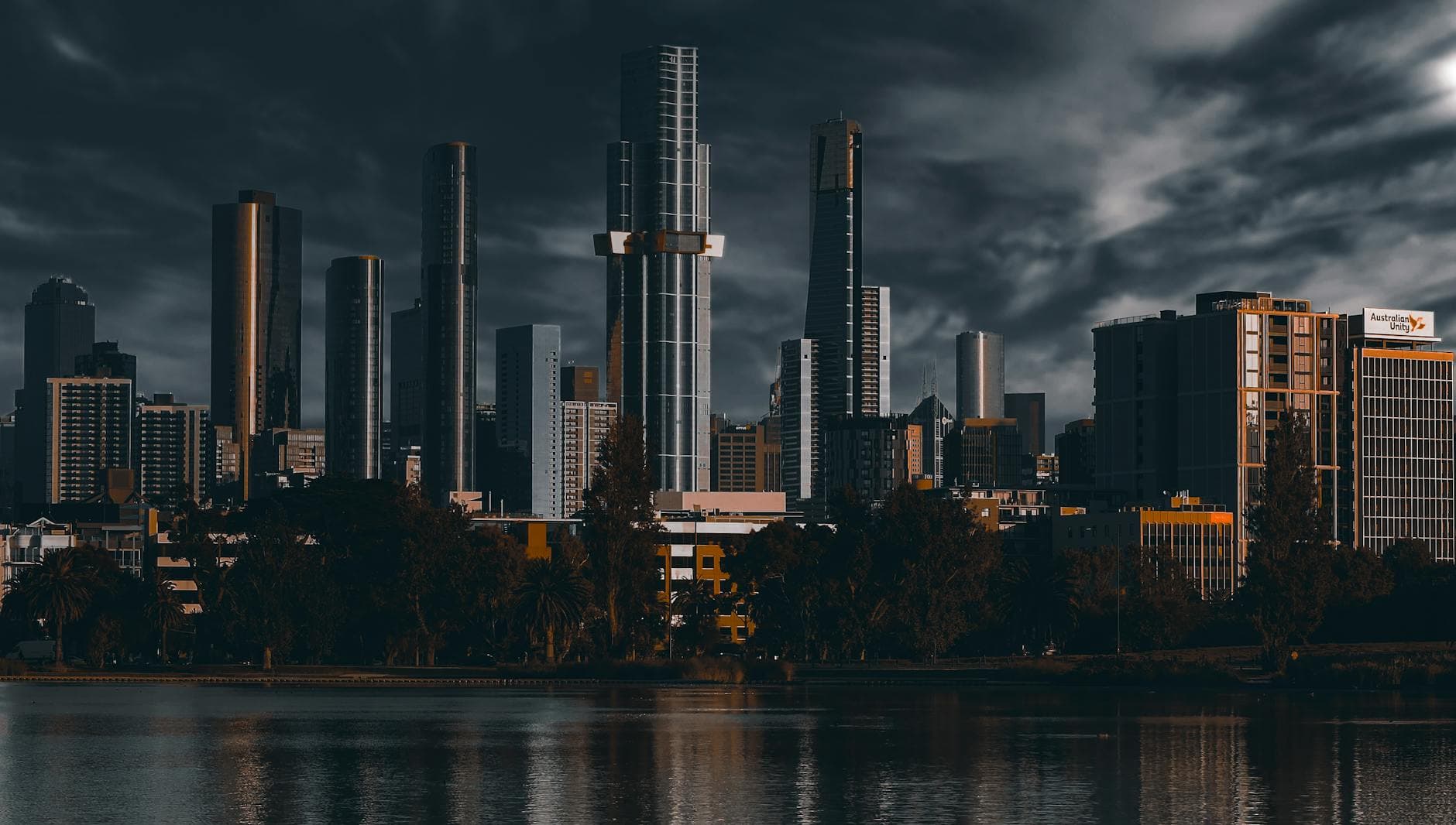 Melbourne's dramatic skyline reflected in the waterfront under moody skies.