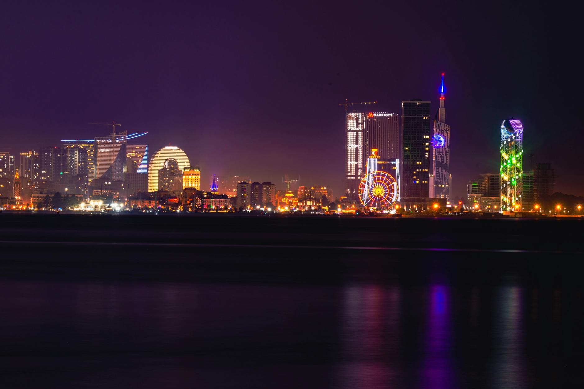 Explore the illuminated Batumi skyline featuring colorful skyscrapers and a Ferris wheel along the Black Sea waterfront.