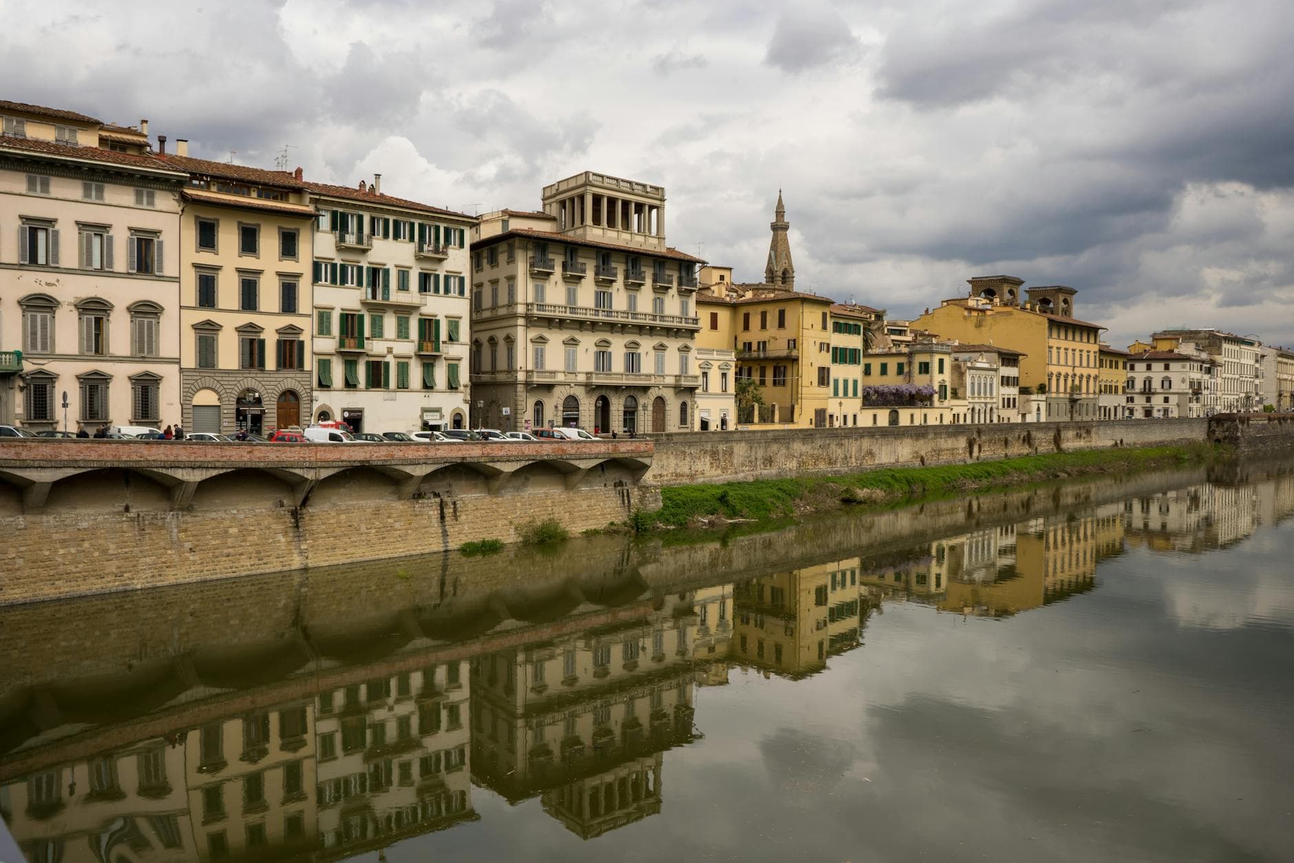 Scenic view of historic buildings reflected in the river in Florence, Italy under cloudy skies.