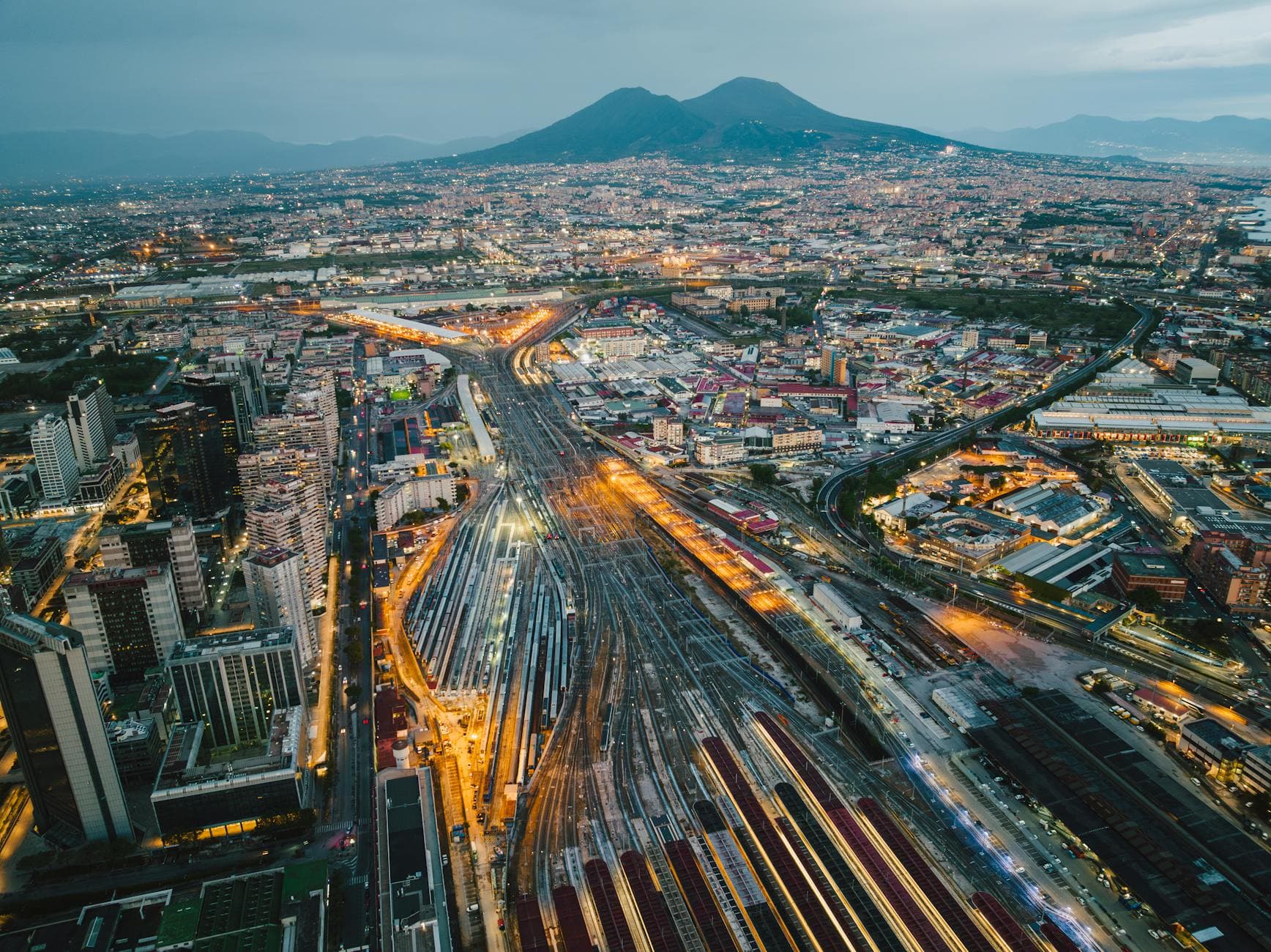 Stunning aerial view of Naples cityscape with Mount Vesuvius at dusk showcasing illuminated streets and urban architecture.