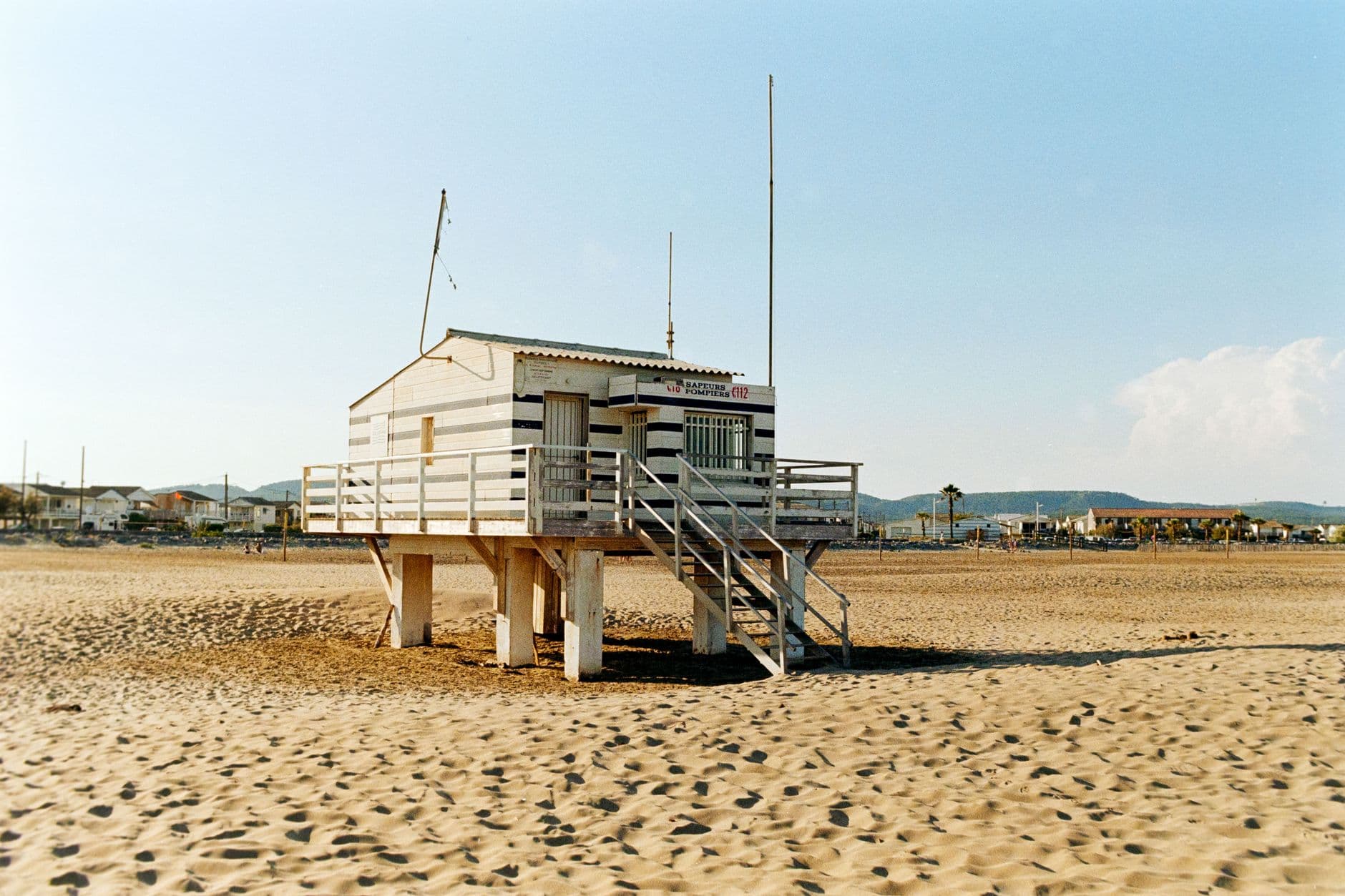 A scenic view of a lifeguard tower on a sandy beach in Gruissan, Occitanie, France, under a clear blue sky.