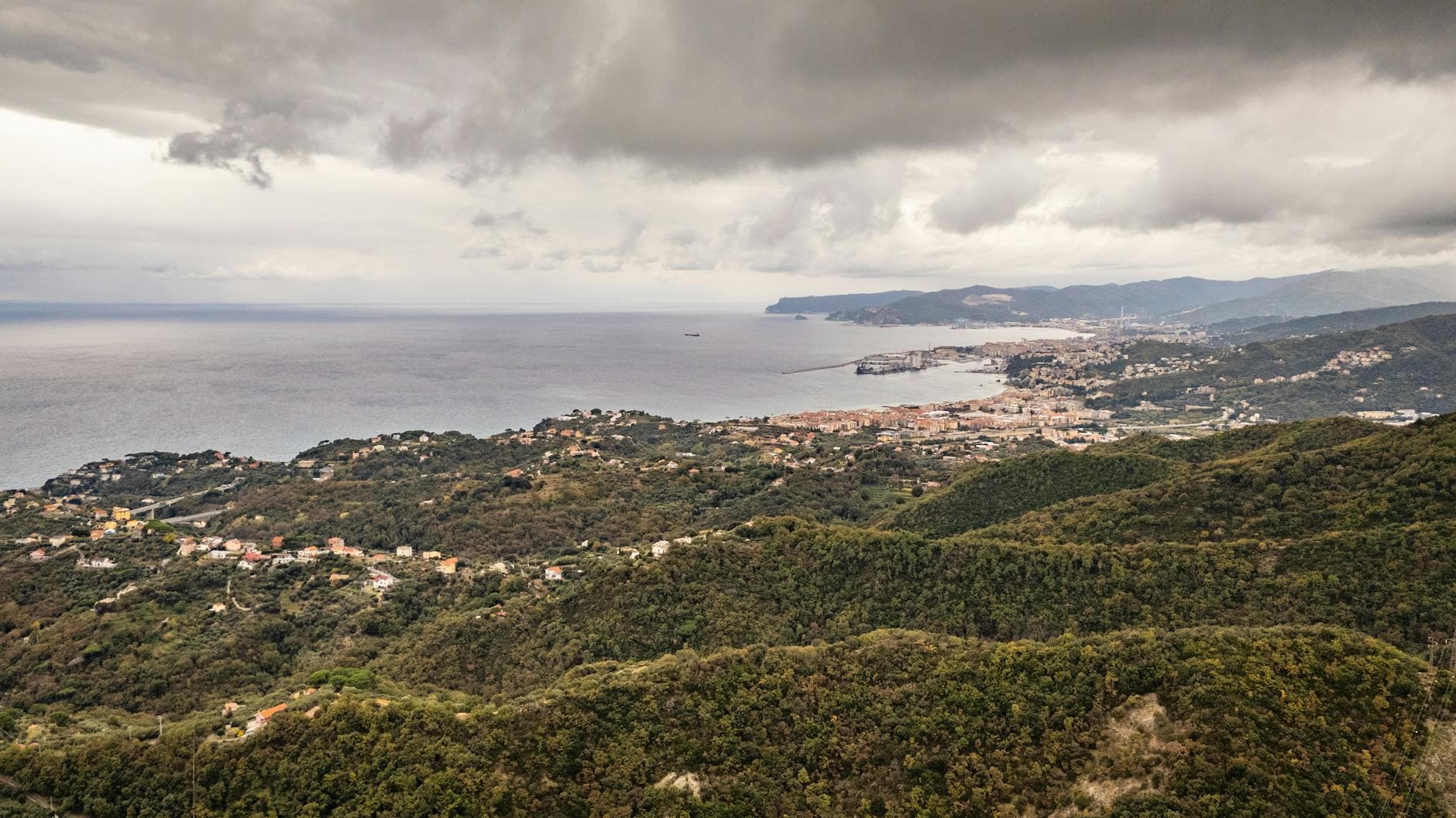 Scenic aerial view of Gameragna, Liguria, Italy with lush hills and coastal landscape under cloudy skies.