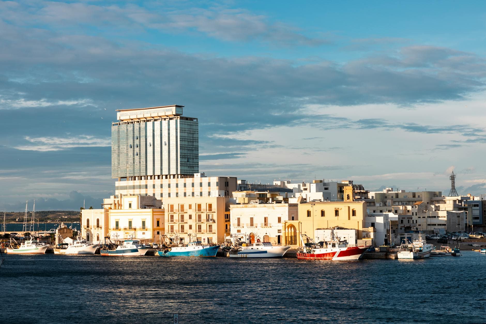 Vibrant coastal view of Gallipoli, Italy with buildings and moored boats under a bright sky.