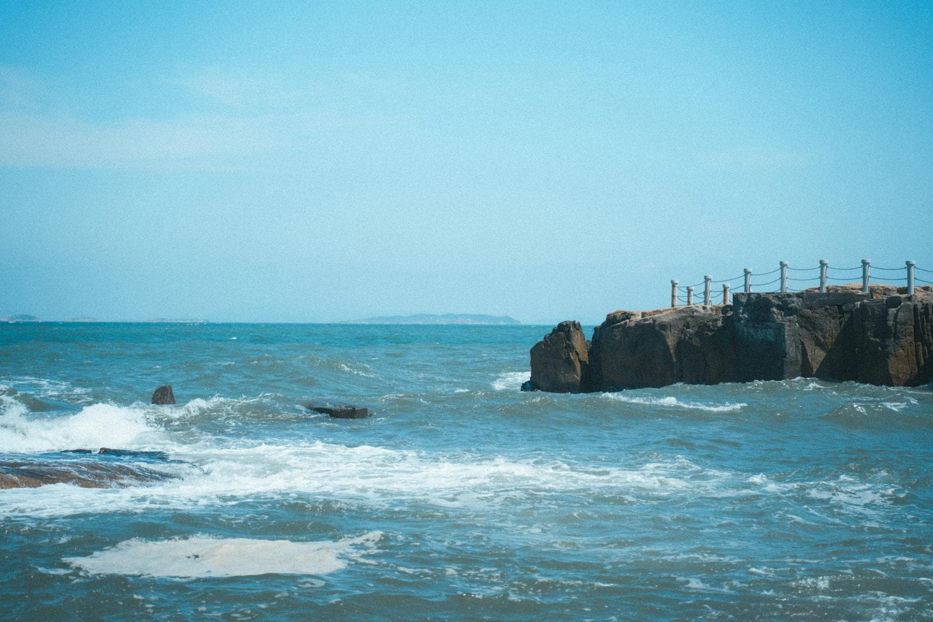 A tranquil view of a rocky shore with waves crashing on a sunny day.