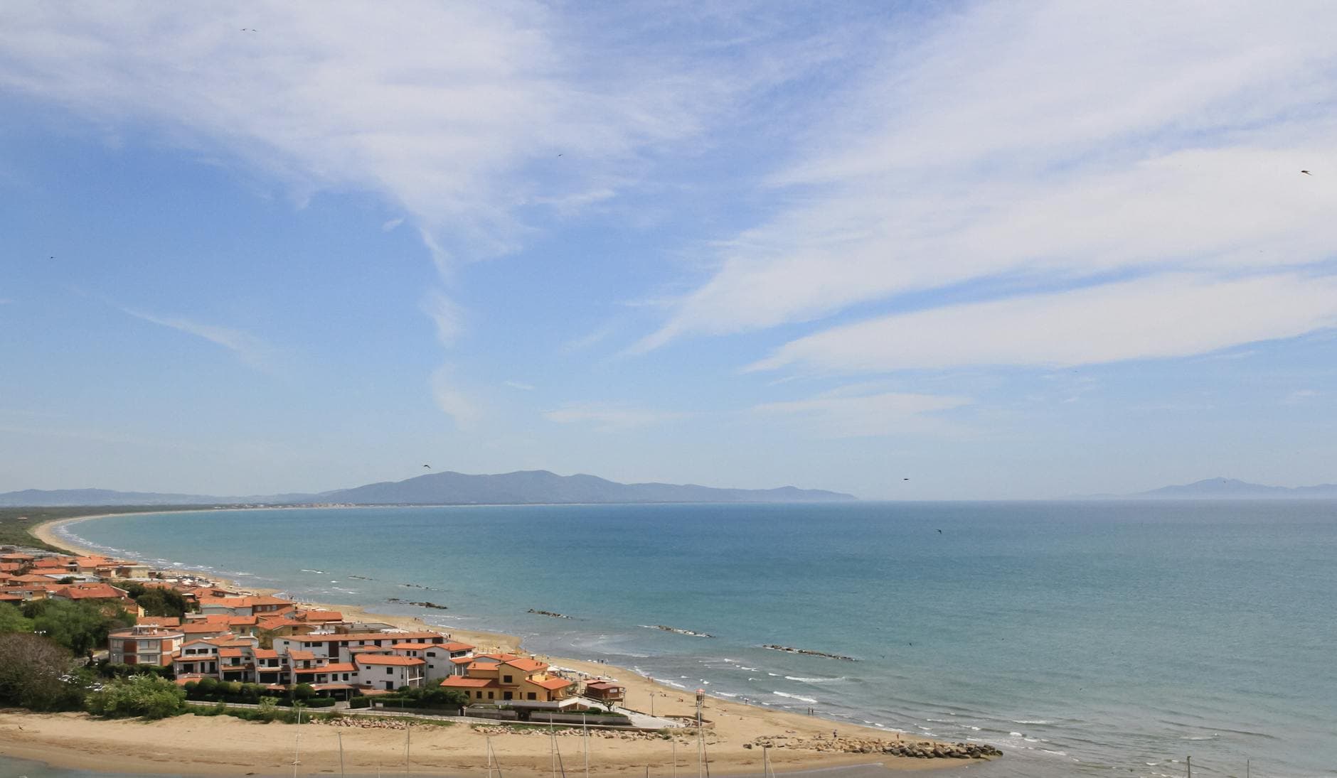 A scenic coastal village with orange rooftops by the tranquil azure sea under a bright sky.