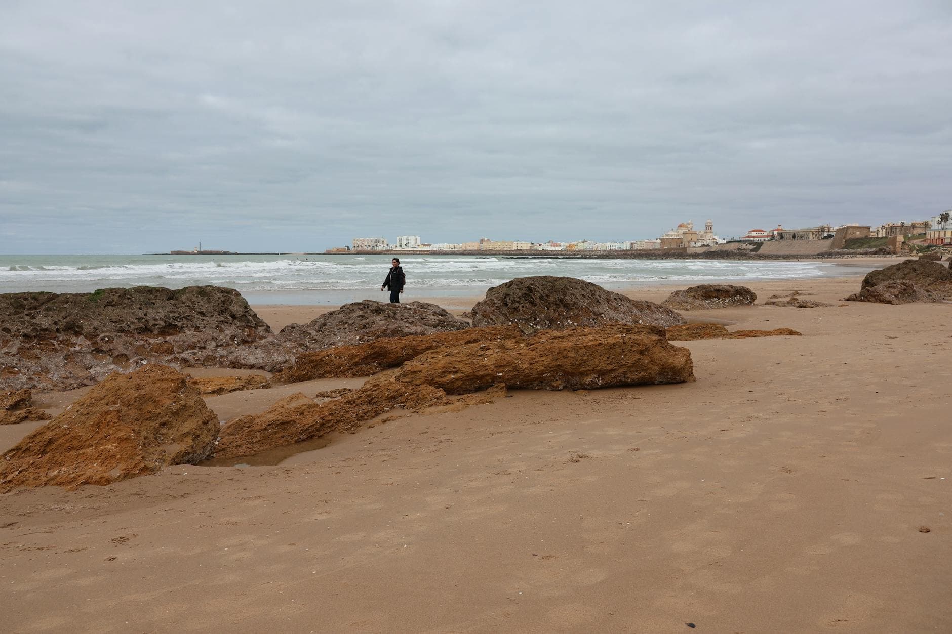 Explore the historic cityscape of Cádiz from a sandy beach with rocky shorelines and ancient walls.