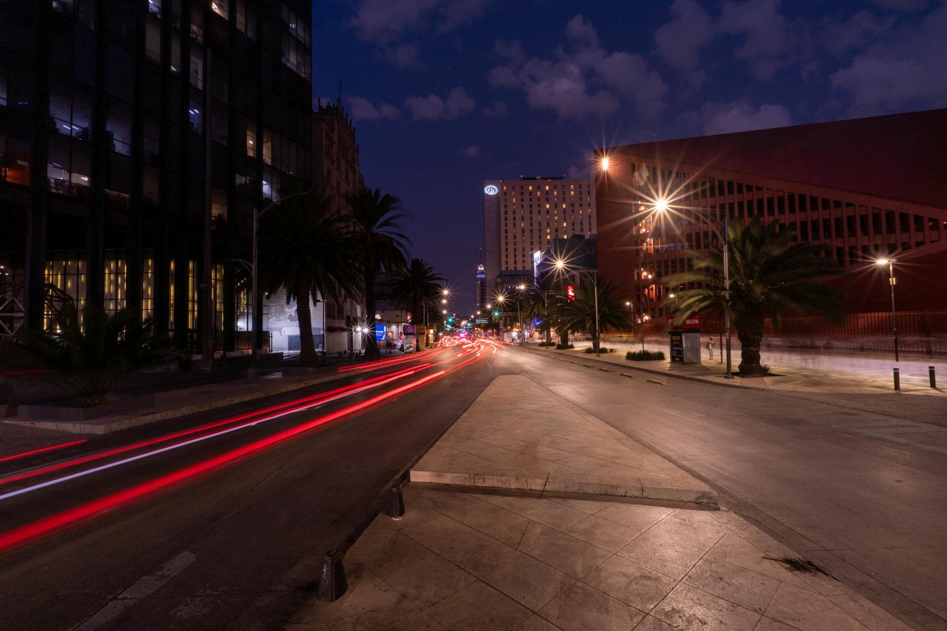 Capture of a bustling Mexico City street at night, featuring prominent light trails and architectural details.