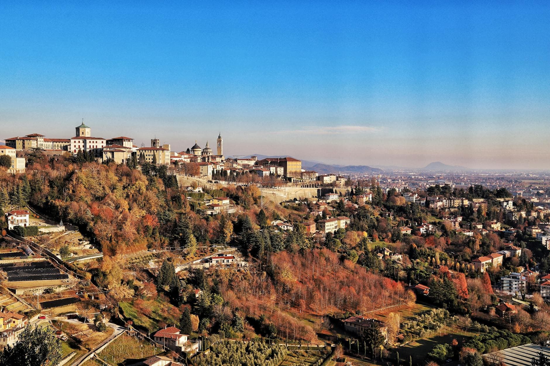 Stunning aerial capture of Bergamo, showcasing its historic architecture and vibrant autumn foliage.