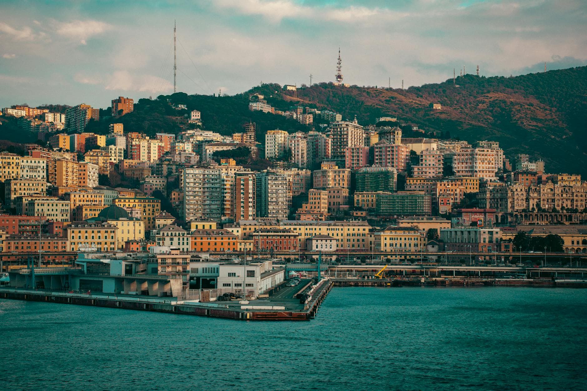 Scenic shot of Genoa's vibrant coastal skyline with colorful buildings against a hilly backdrop.