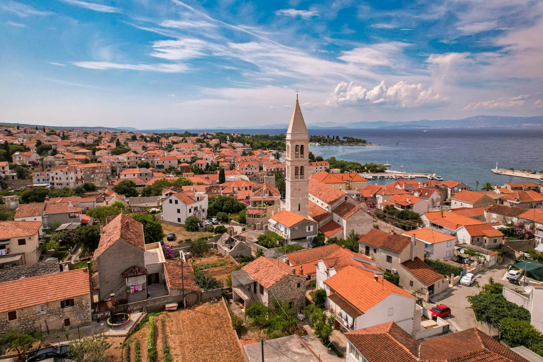 A picturesque aerial view of a coastal town in Croatia with red-roofed buildings and a prominent church tower.