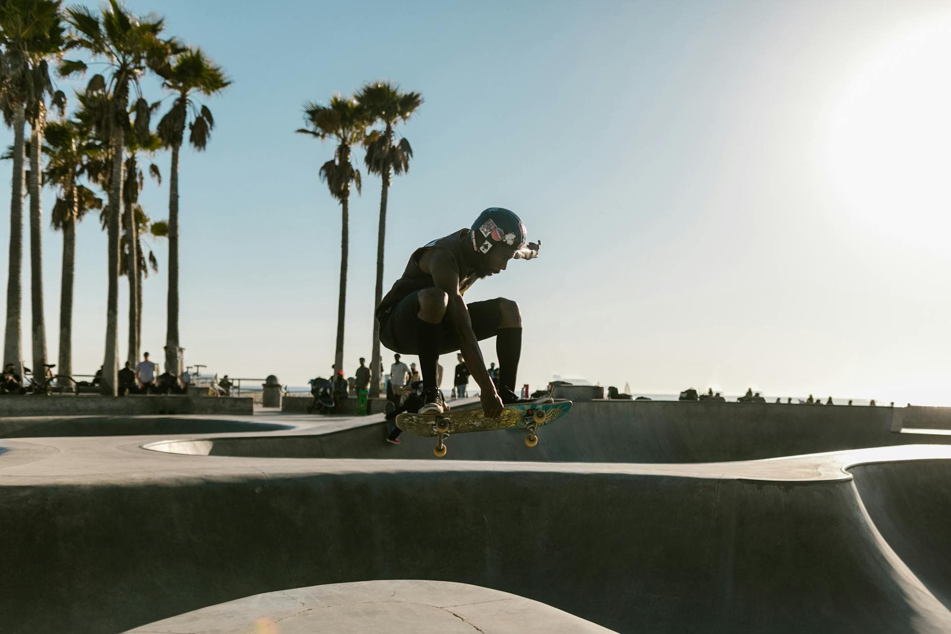 A skateboarder performs an aerial trick in the vibrant Venice Beach skatepark under a sunny sky.