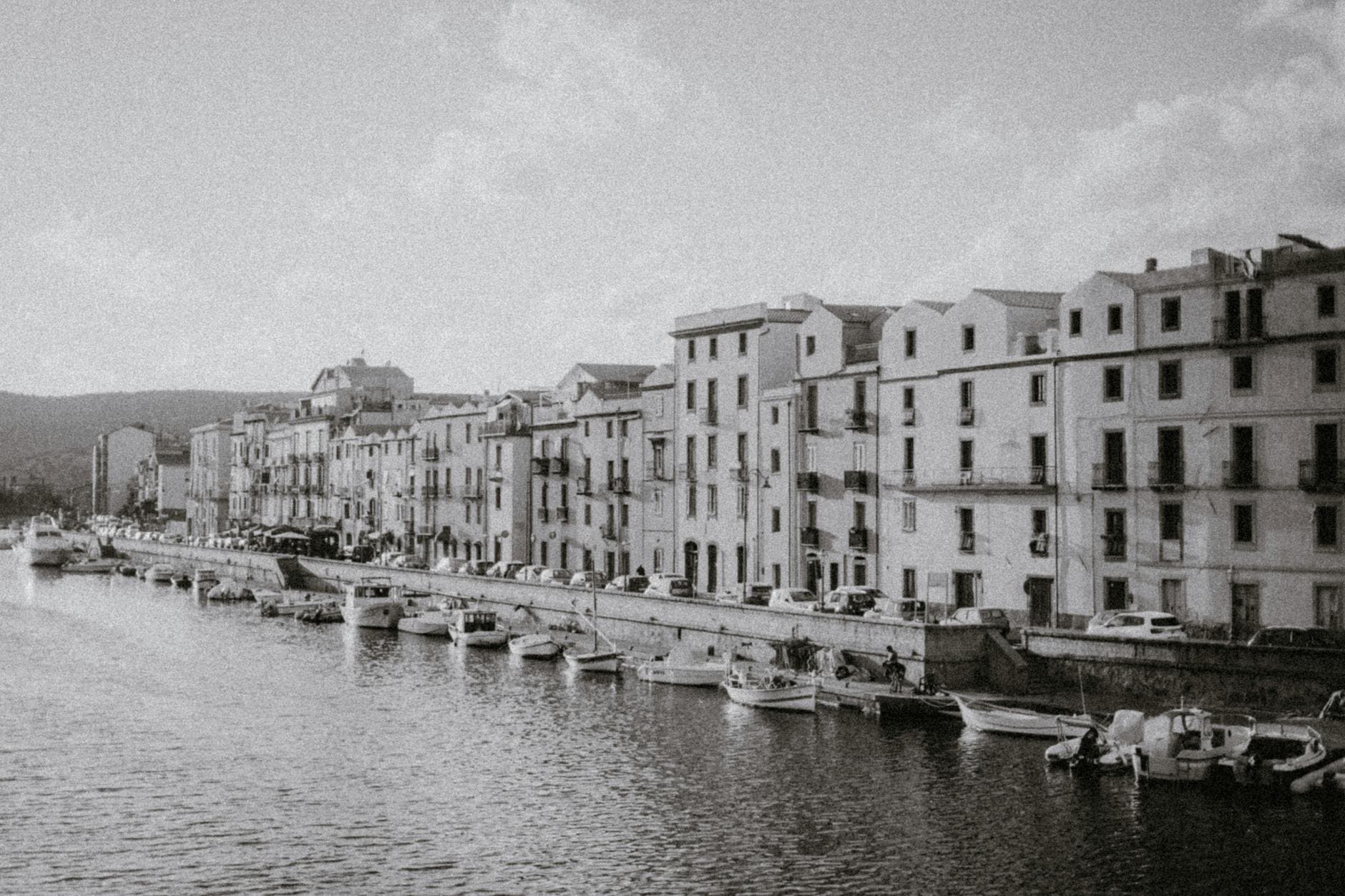 Black and white image capturing scenic waterfront and historic buildings in an Italian town.