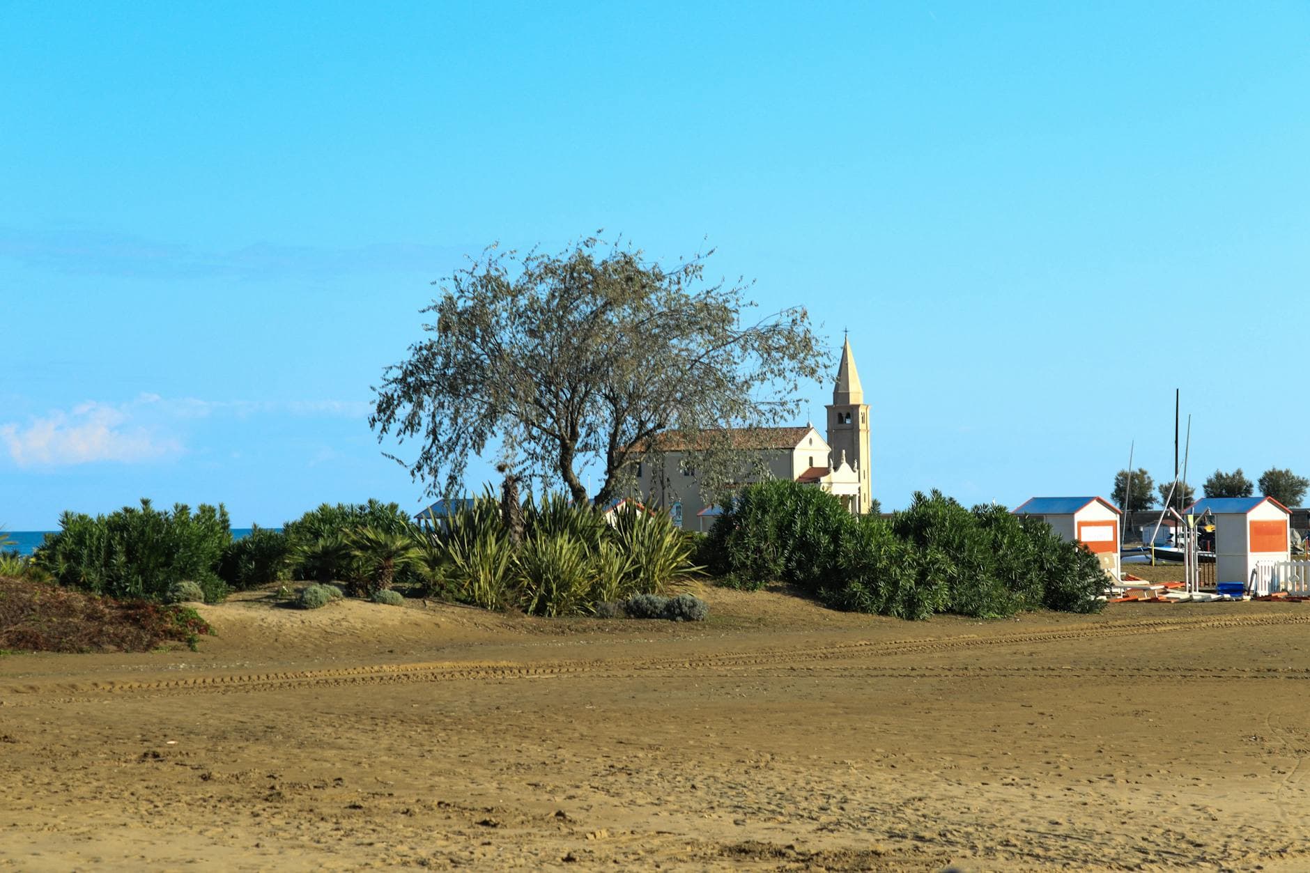 A serene sandy beach with lush greenery and a church in the background under a blue sky.