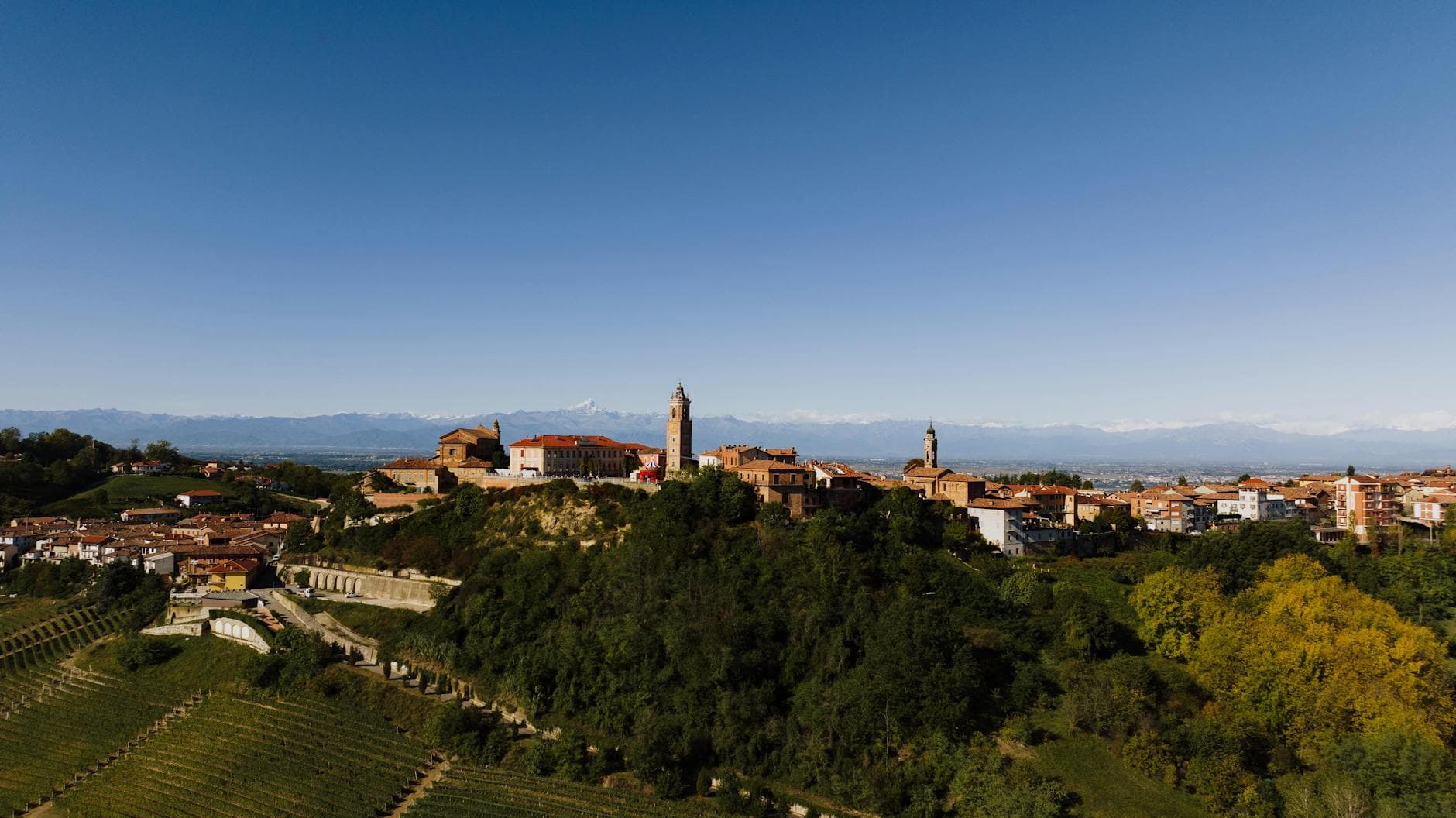 A scenic aerial view of the historic La Morra village in Piemonte, Italy surrounded by vineyards and mountains.