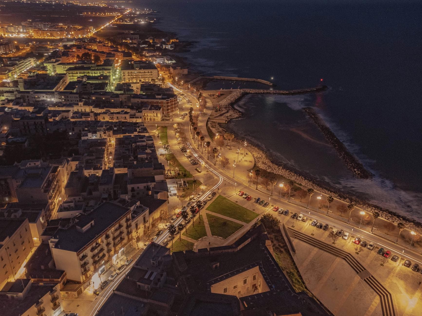 Stunning aerial view of Mola di Bari's waterfront at night with glowing streetlights and a lively townscape along the coast.