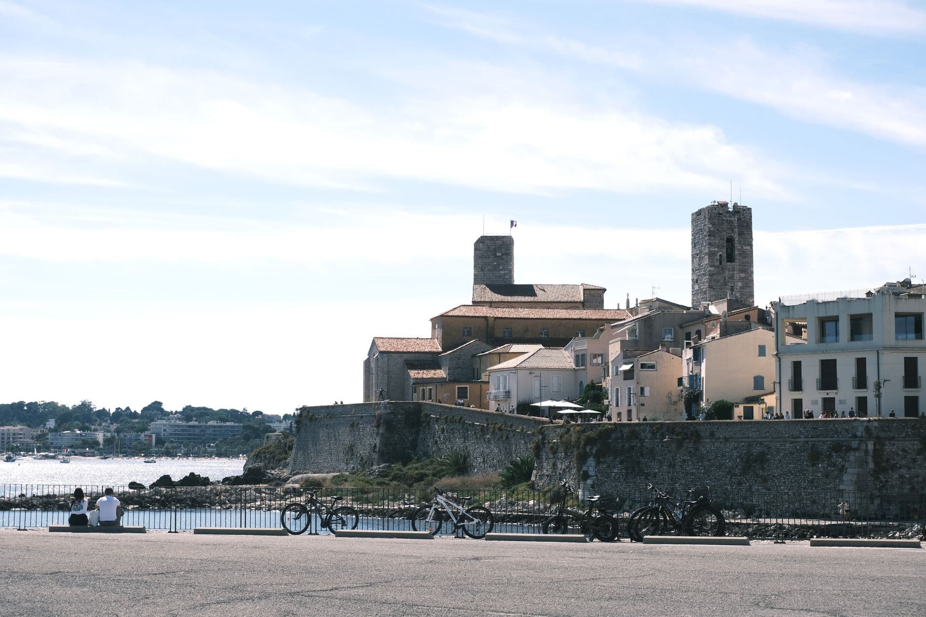 View of historic Antibes with prominent fort tower by the sea, bicycles in foreground.