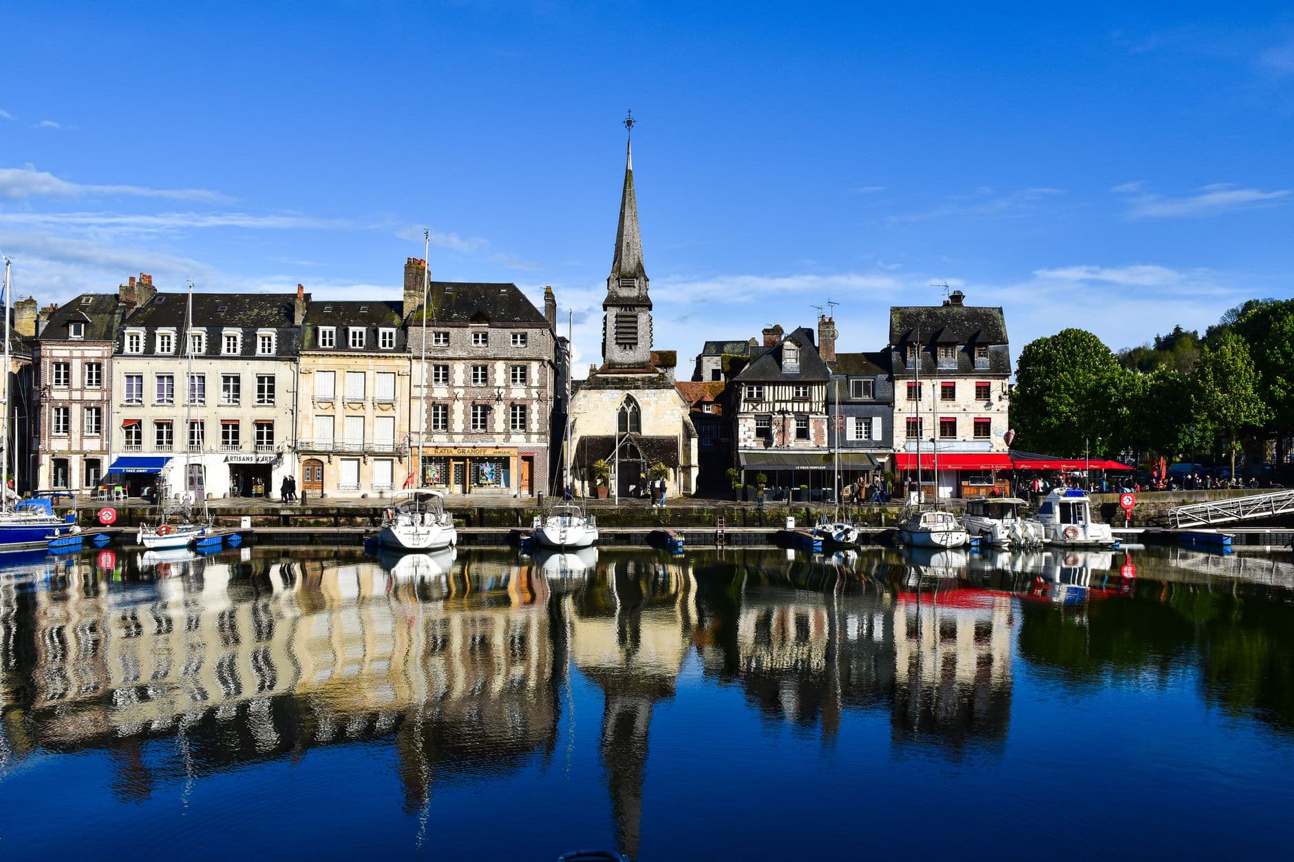 Scenic view of Honfleur's waterfront with historic buildings and calm reflections under a clear blue sky.