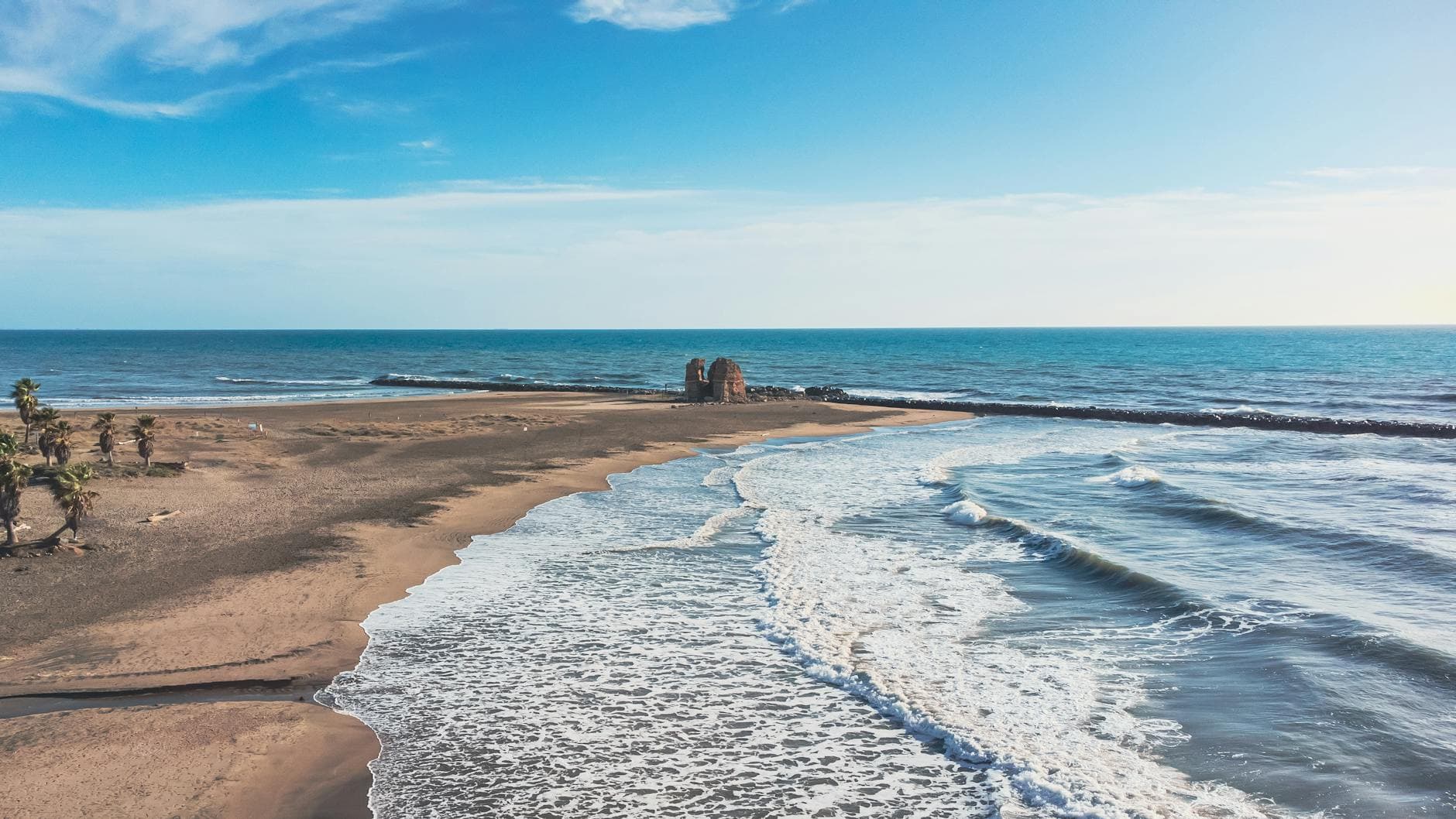 A stunning view of Ladispoli beach, Italy, with waves crashing and a bright blue sky.