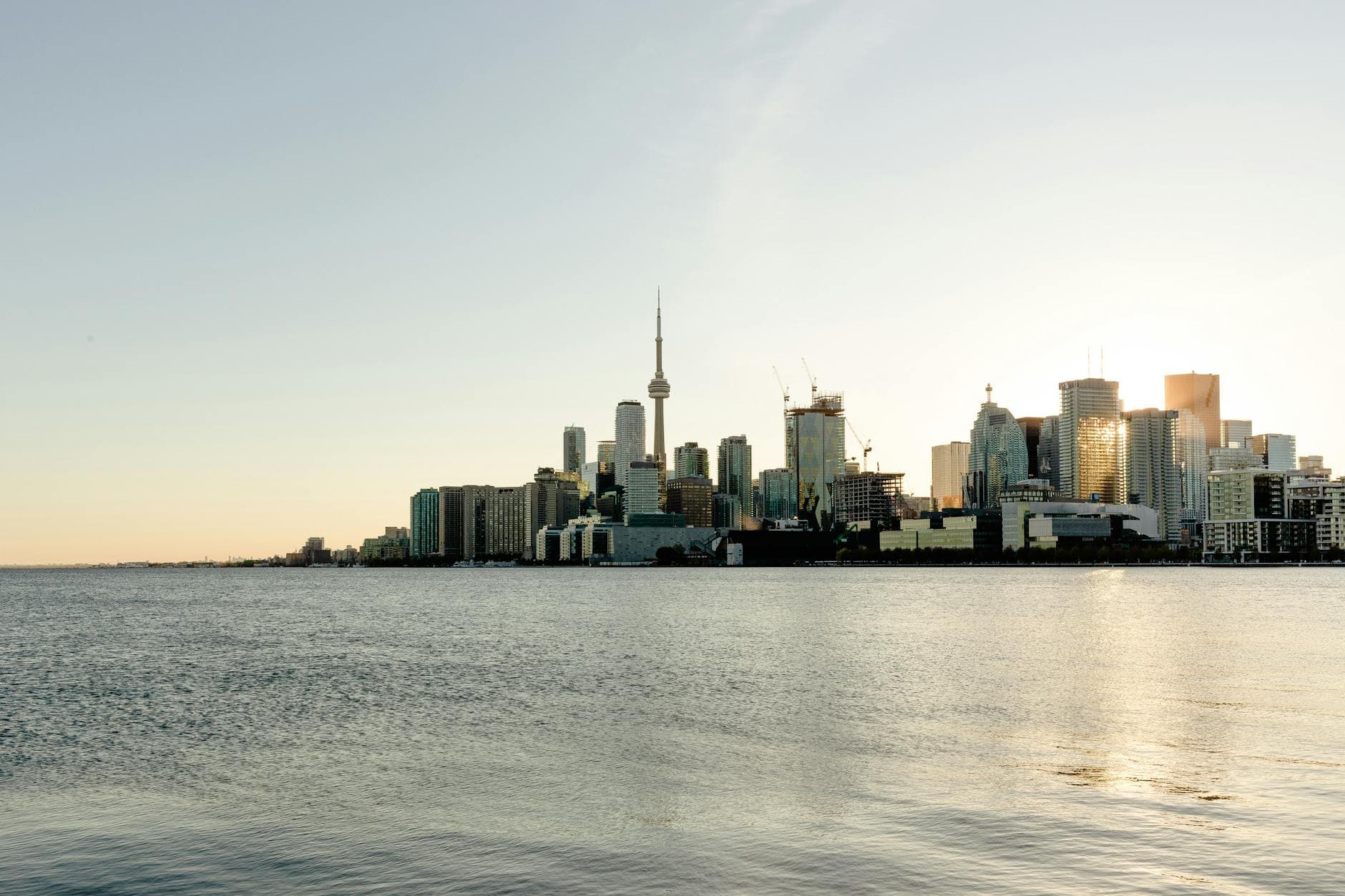 Modern city of Toronto with glass skyscrapers and towers built on seashore under blue sky in early evening