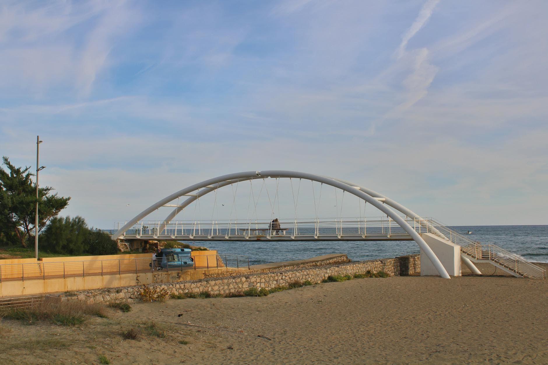 Modern white arch bridge spans a sandy beach along the ocean in Latina, Italy.