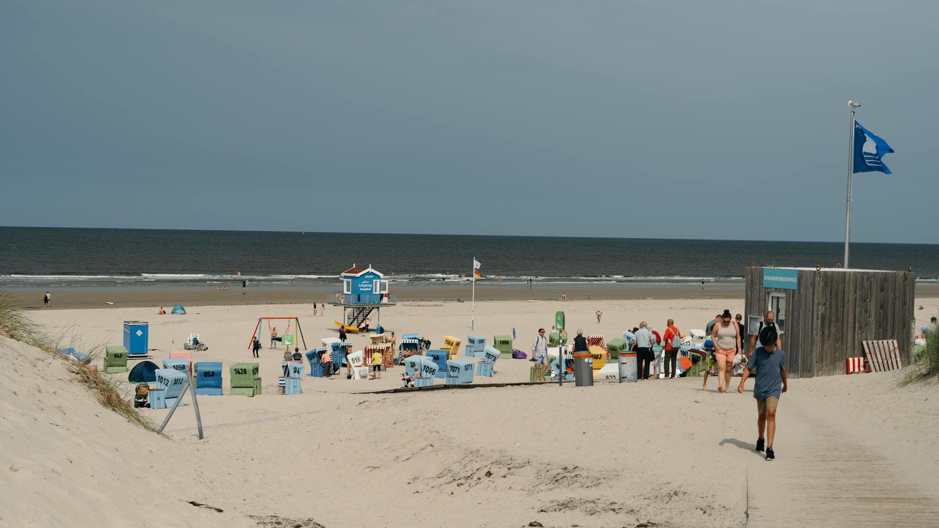 Sunny day at the beach with people, colorful chairs, and lifeguard tower in view.