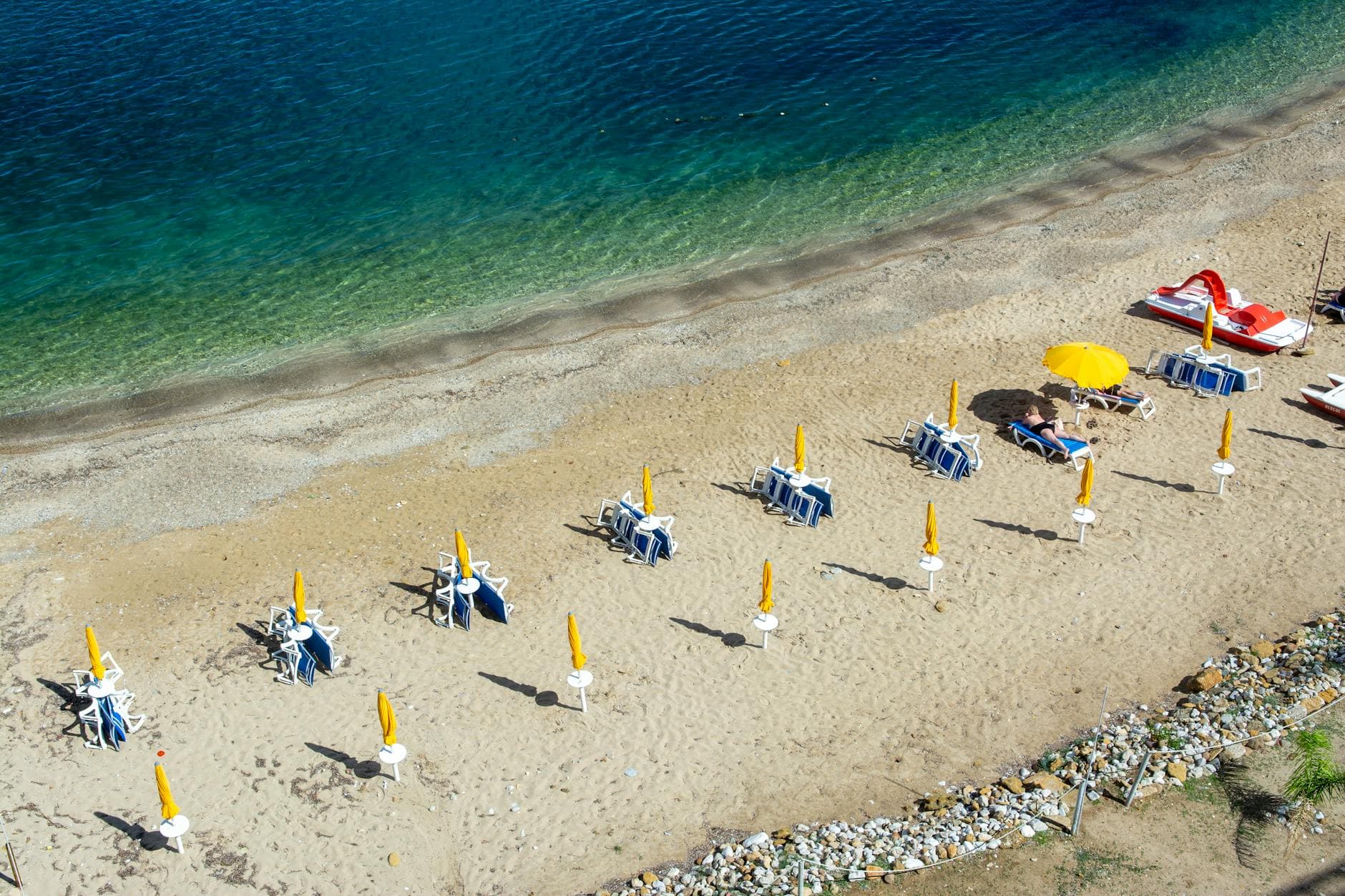 Aerial view of serene sandy beach with yellow umbrellas and clear blue sea in Sicily, Italy.