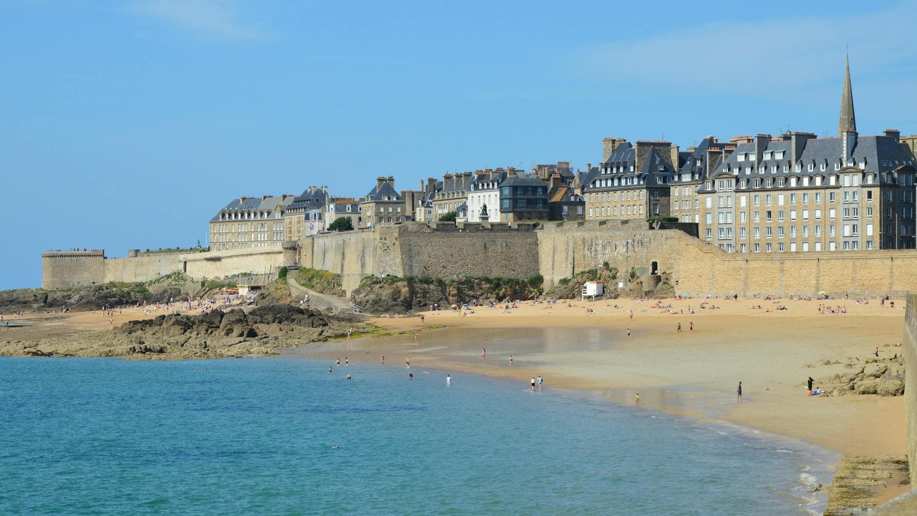 A picturesque beach scene in Saint-Malo, Bretagne, France with historic buildings and blue waters.