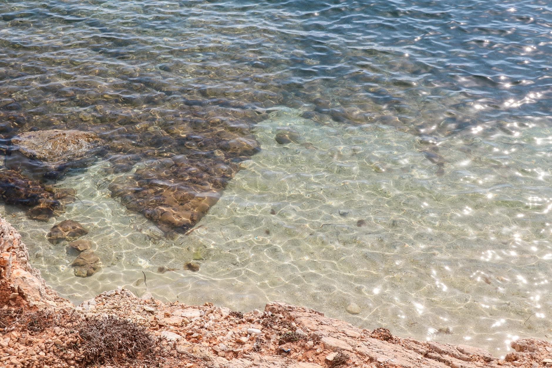 A serene view of clear blue water and rocky shoreline in Sicilia, Italy.