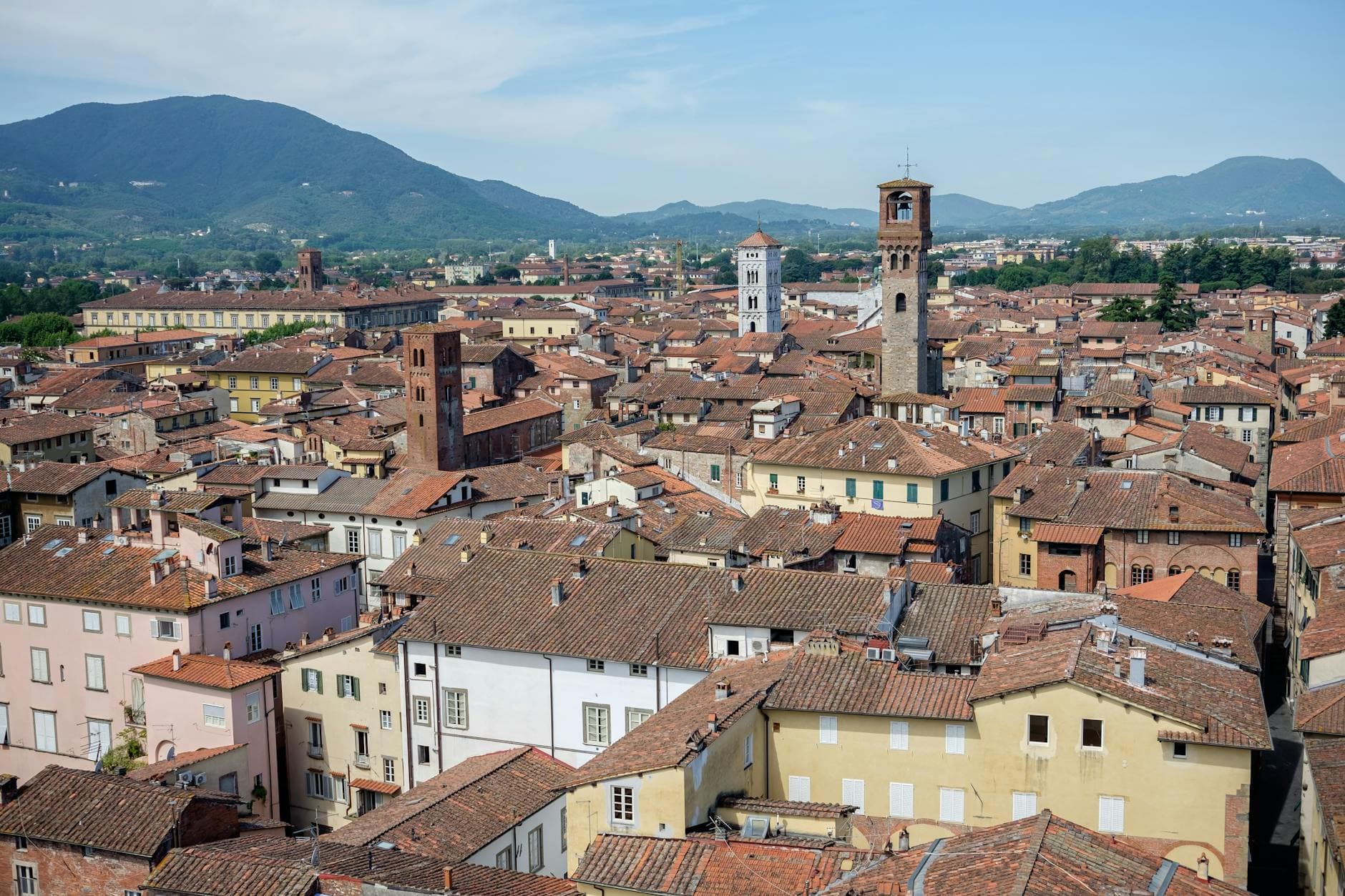 Explore the charming rooftops and towers of historic Lucca, Italy, set against a backdrop of scenic Tuscan mountains.