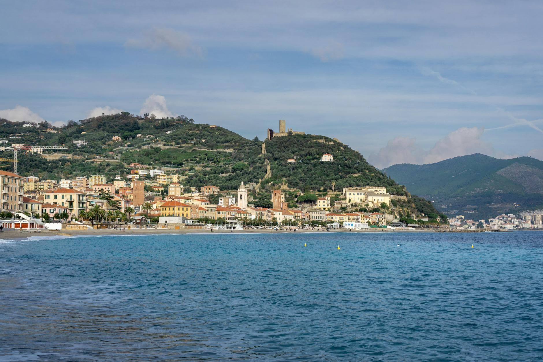 Picturesque view of Noli's coastline in Liguria, Italy, featuring historical castle and lush hills.