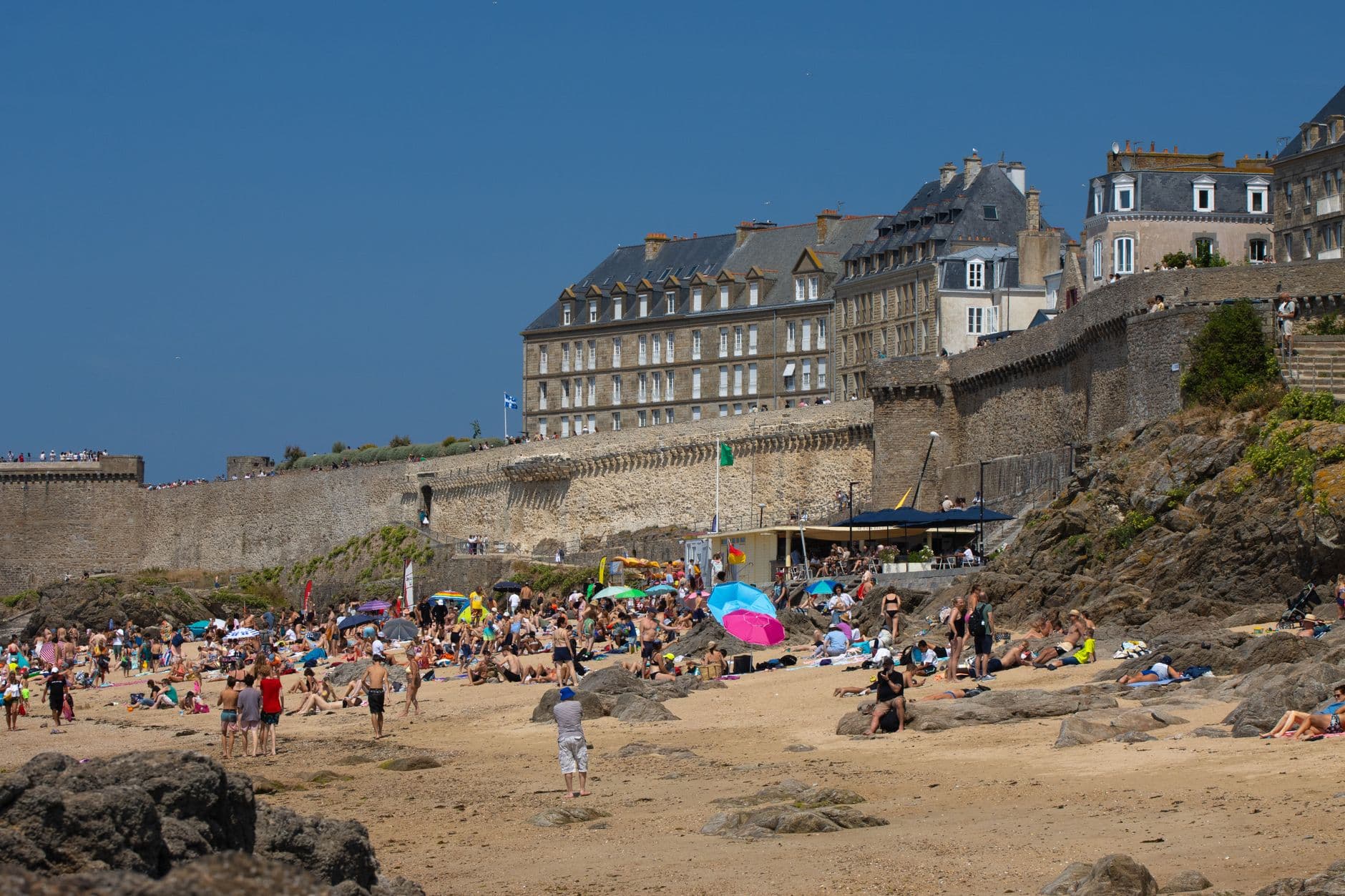 Vibrant beach day at Saint-Malo, France, with historic fortress backdrop and tourists sunbathing.