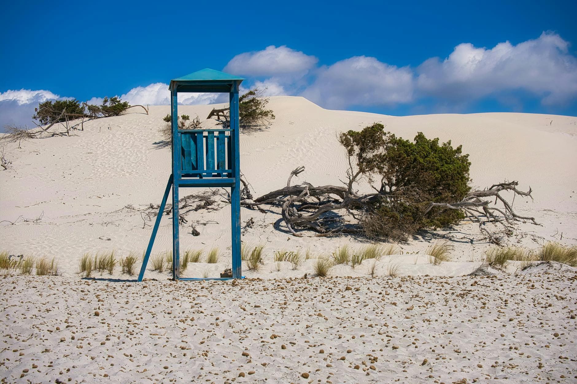 A striking view of white sand dunes with a blue lifeguard tower against a bright blue sky.