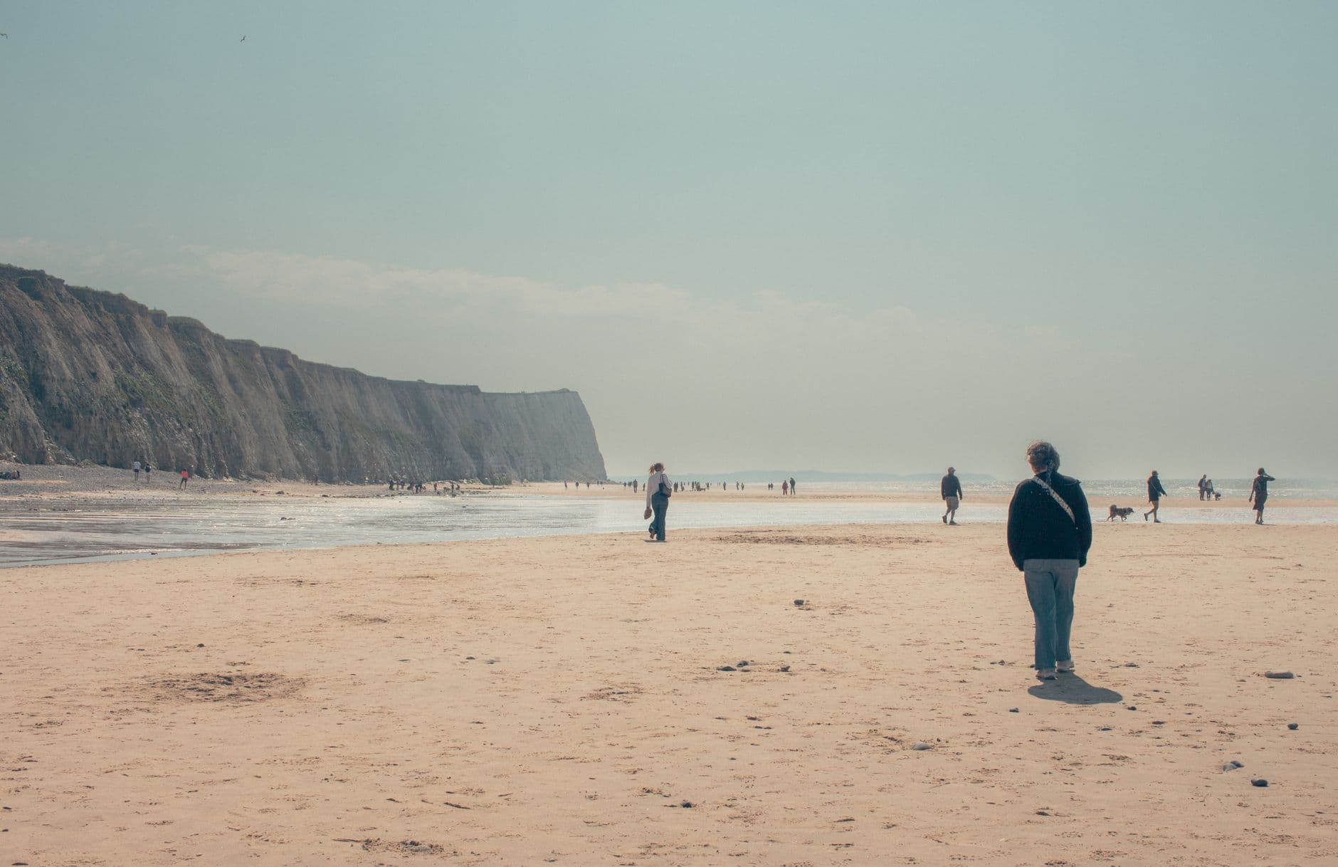 Tranquil beach scene with people walking and cliffs in Hauts-de-France.