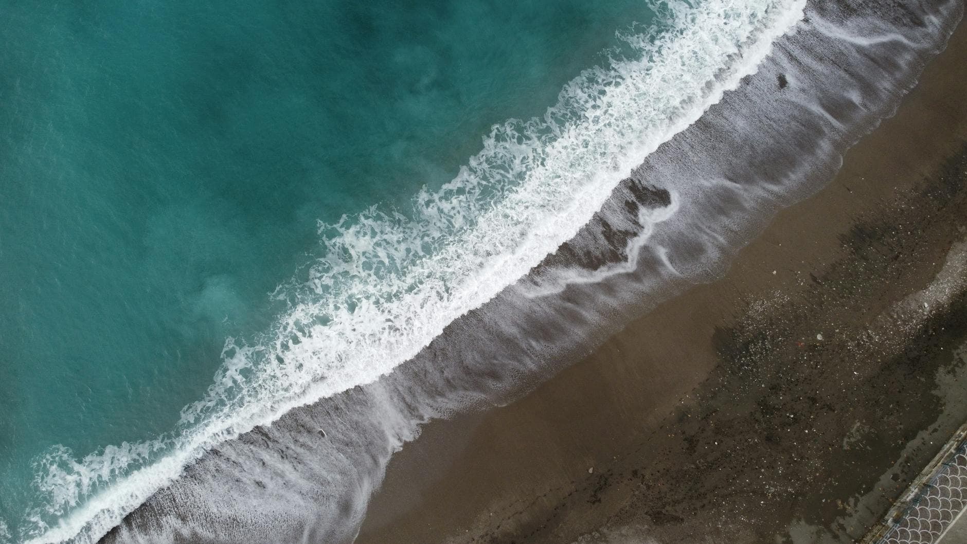 Aerial view of waves crashing on the shoreline in Sorrento, Italy, showcasing pristine beach and turquoise waters.