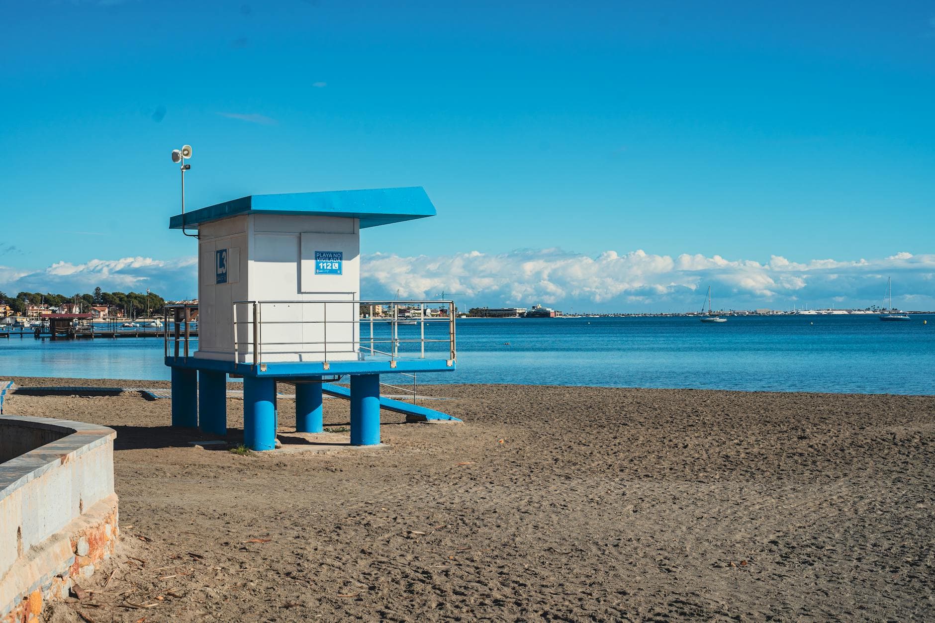 A peaceful beach scene featuring a lifeguard tower by calm sea waters under a clear blue sky.