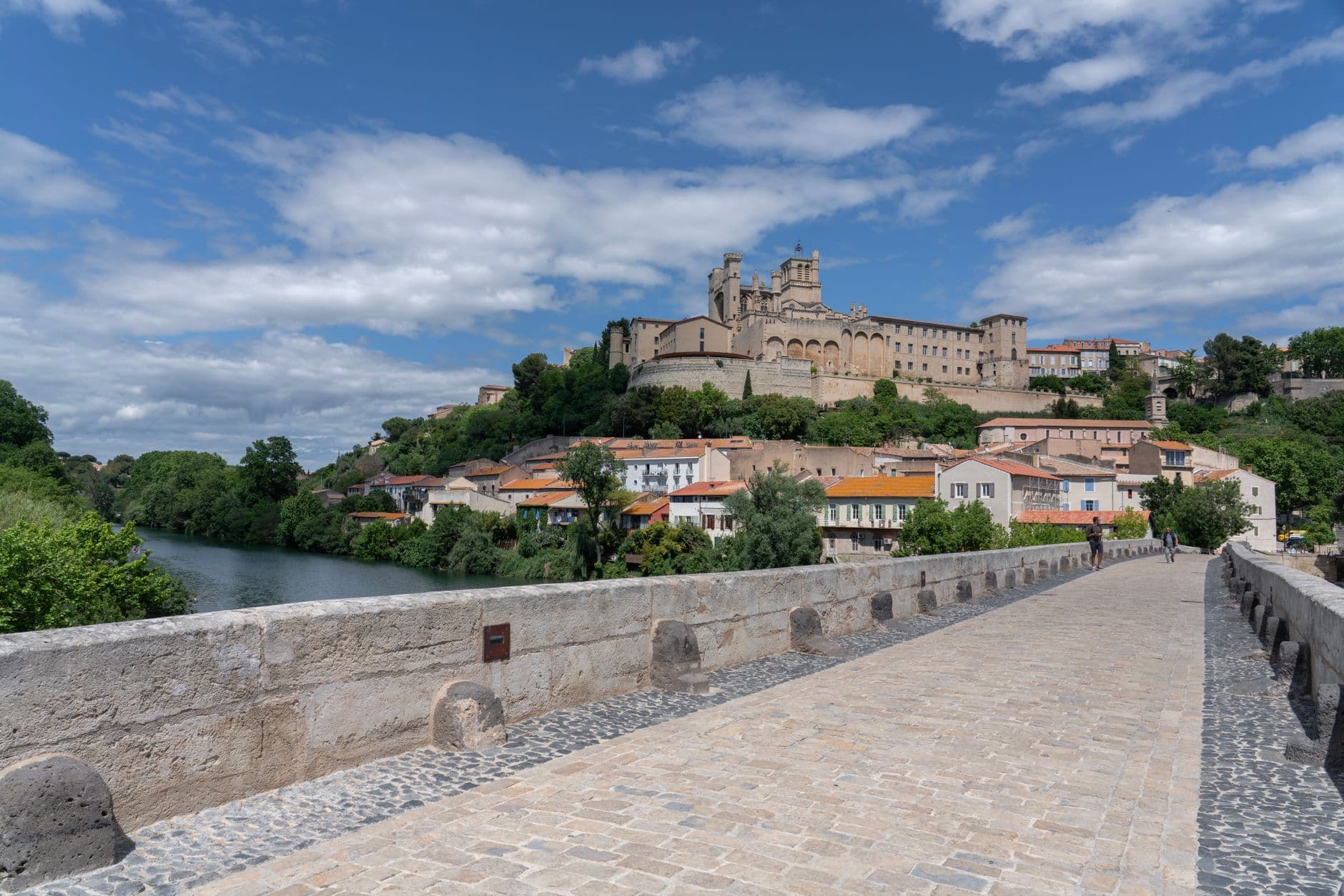 A picturesque view of Beziers Cathedral atop a hill with a historic stone bridge in France's Languedoc region.