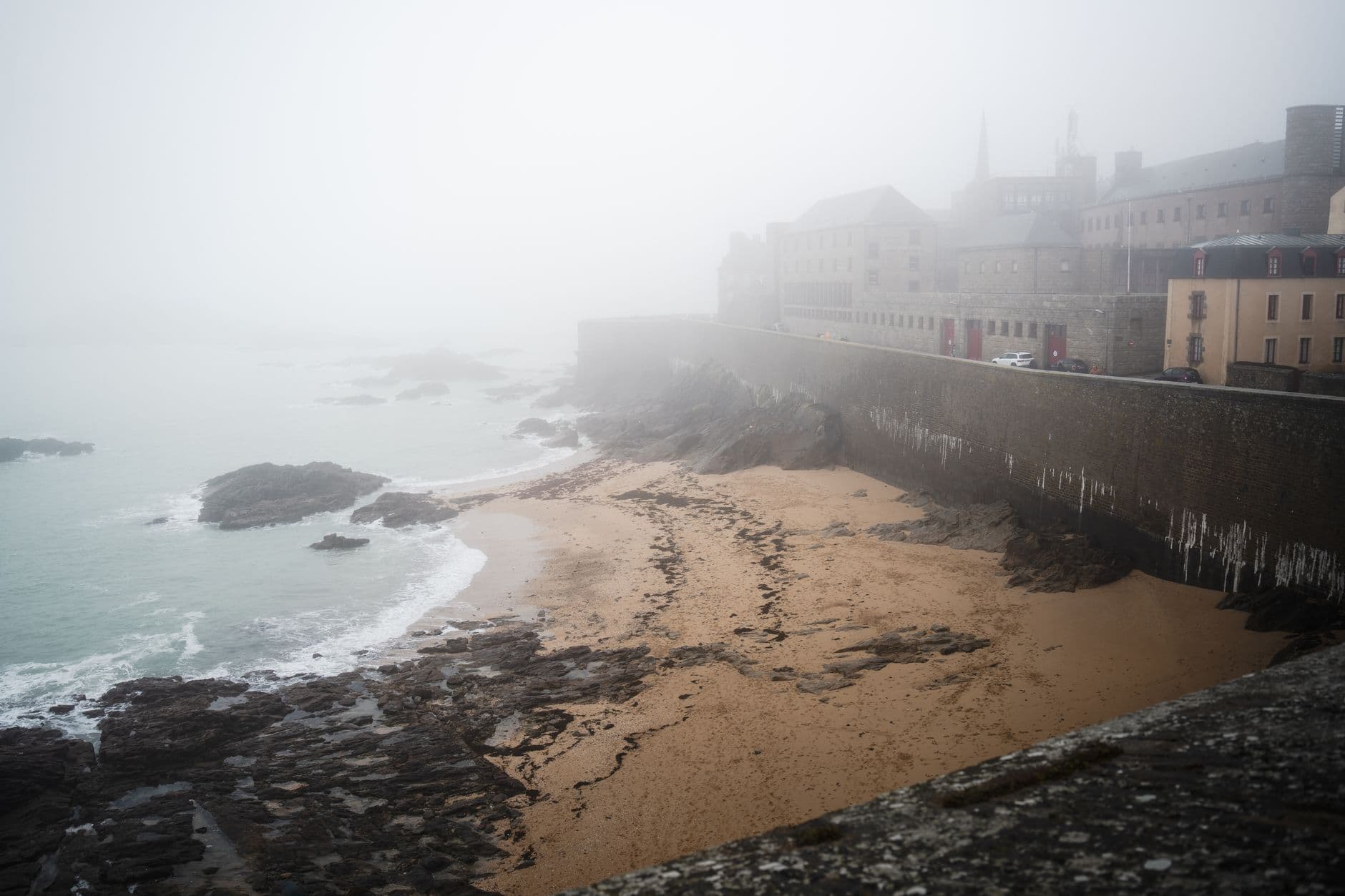 Misty morning view of Saint-Malo's beach in Bretagne, France, with historical fortifications.