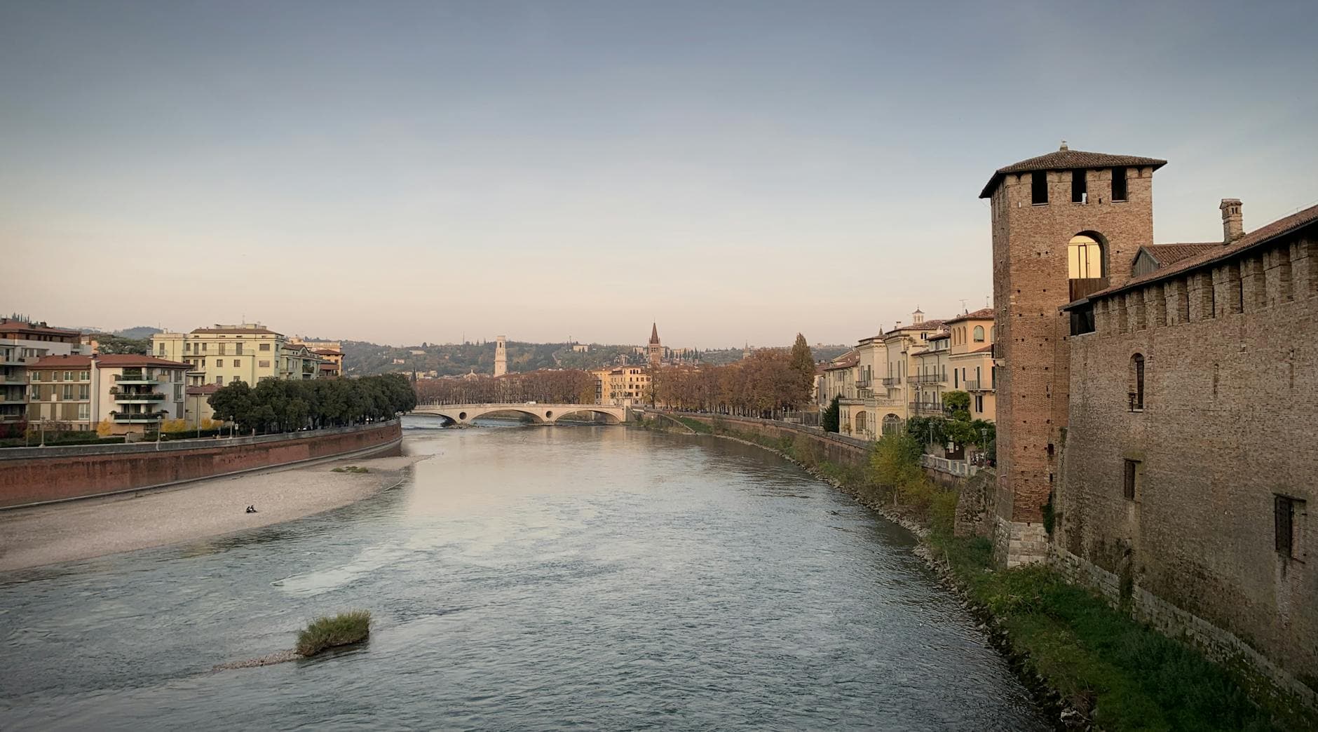 Tranquil river scene with historic bridge and castle at dusk, showcasing serene cityscape.