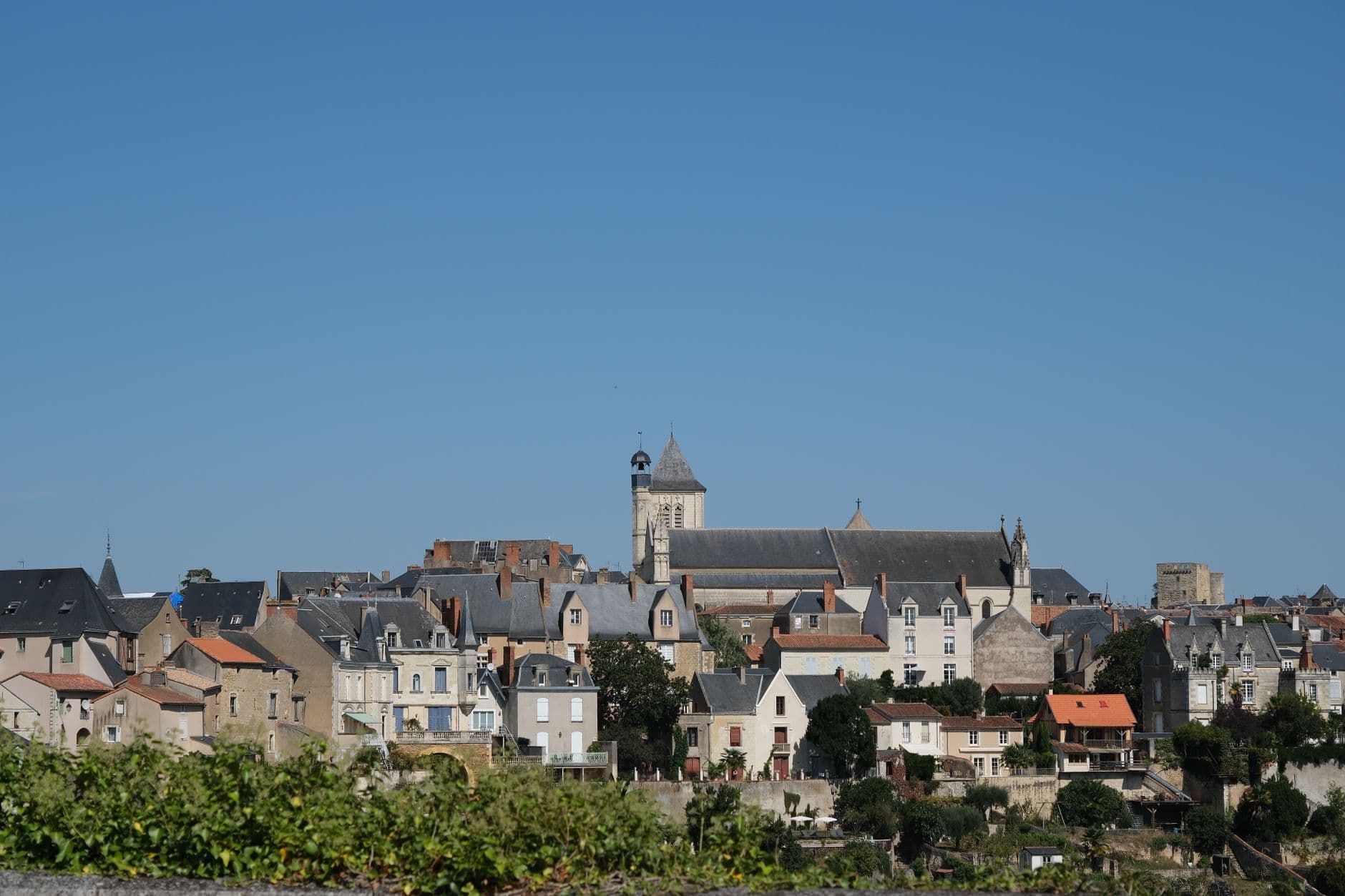 Picturesque view of a charming French town featuring historic buildings and a prominent church under a clear blue sky.