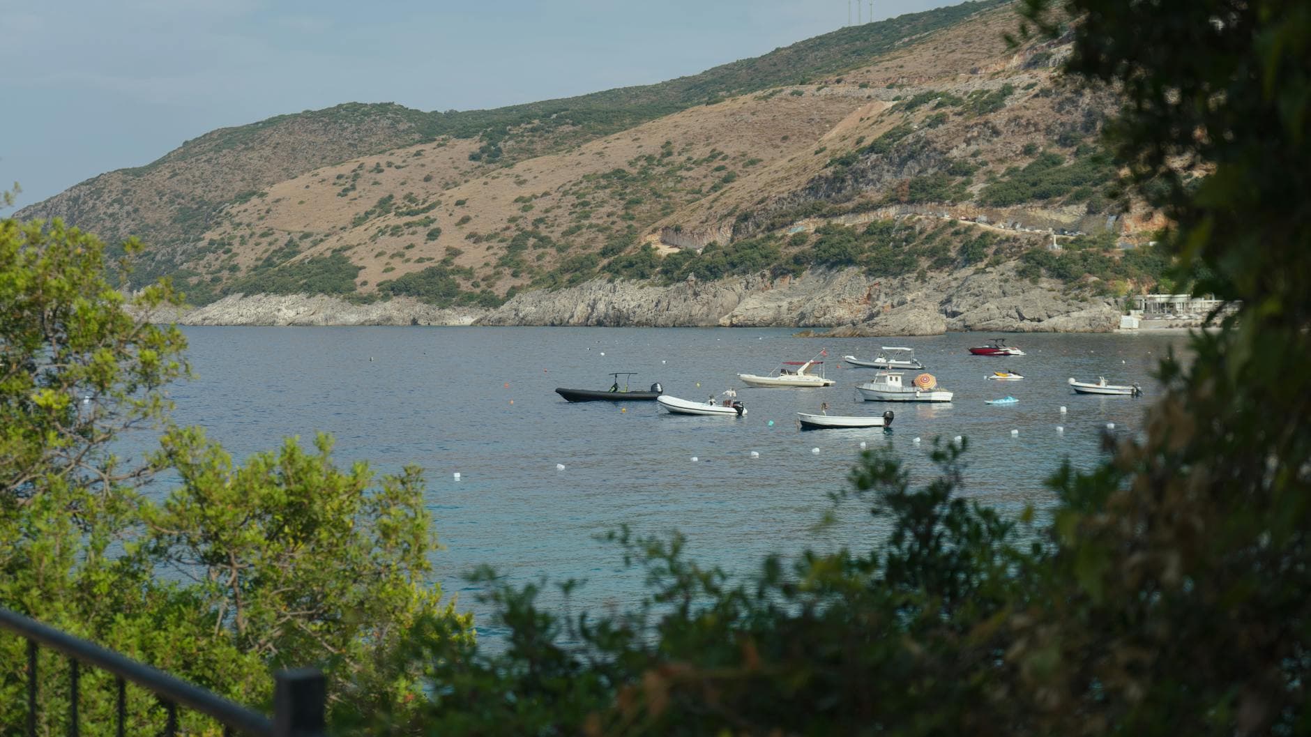 A serene coastal view in Vlorë County, Albania, with boats dotting the tranquil bay under a clear sky.