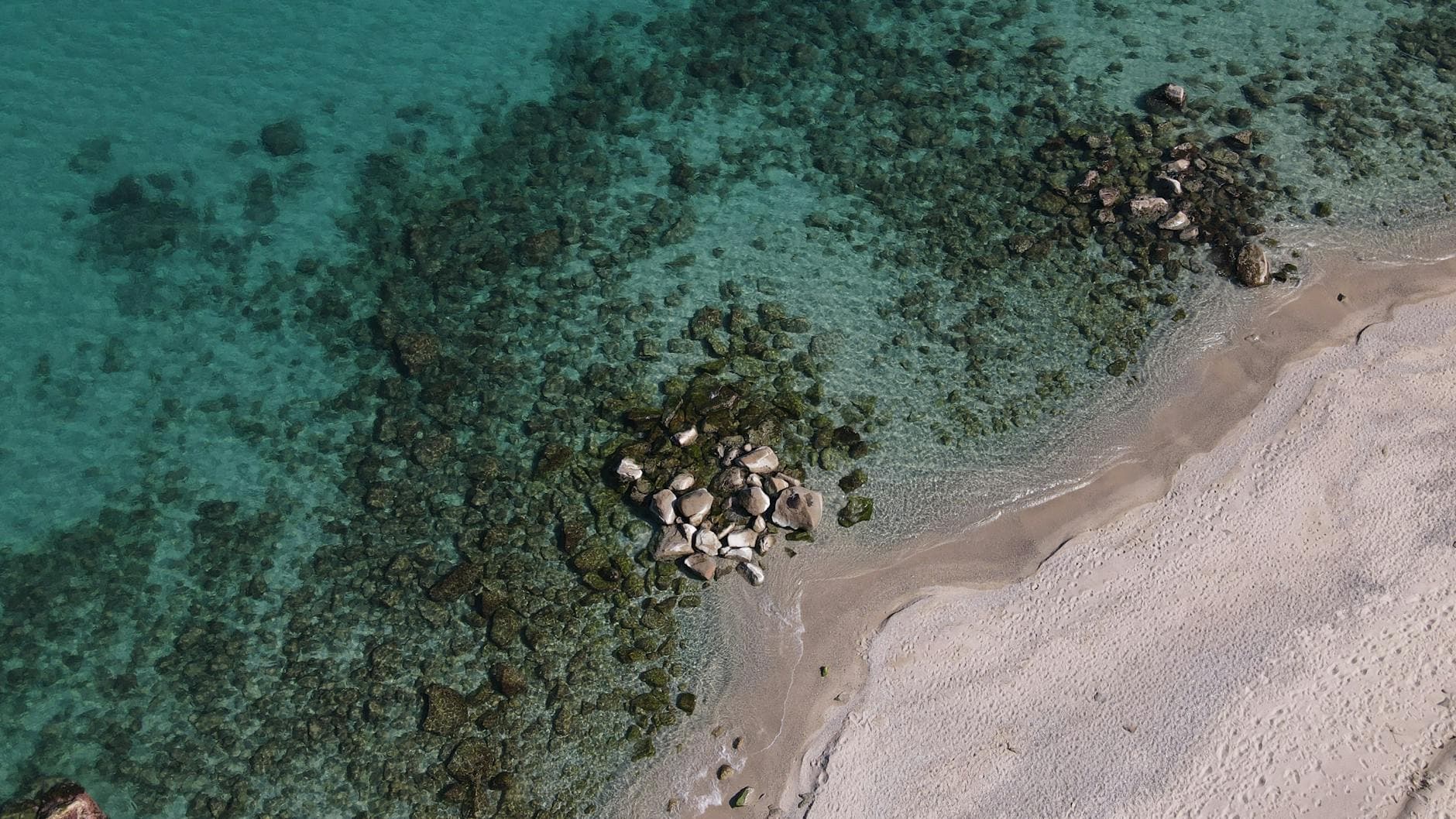Aerial shot of a rocky beach in Soverato, Calabria, Italy with clear turquoise waters.