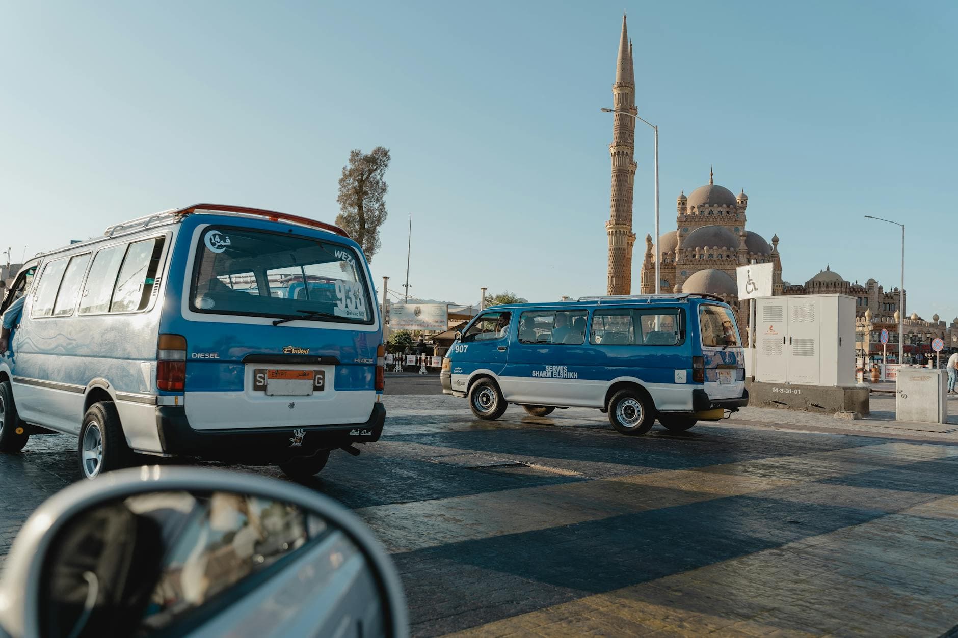 View of a city street featuring a mosque and parked minivans under clear skies.