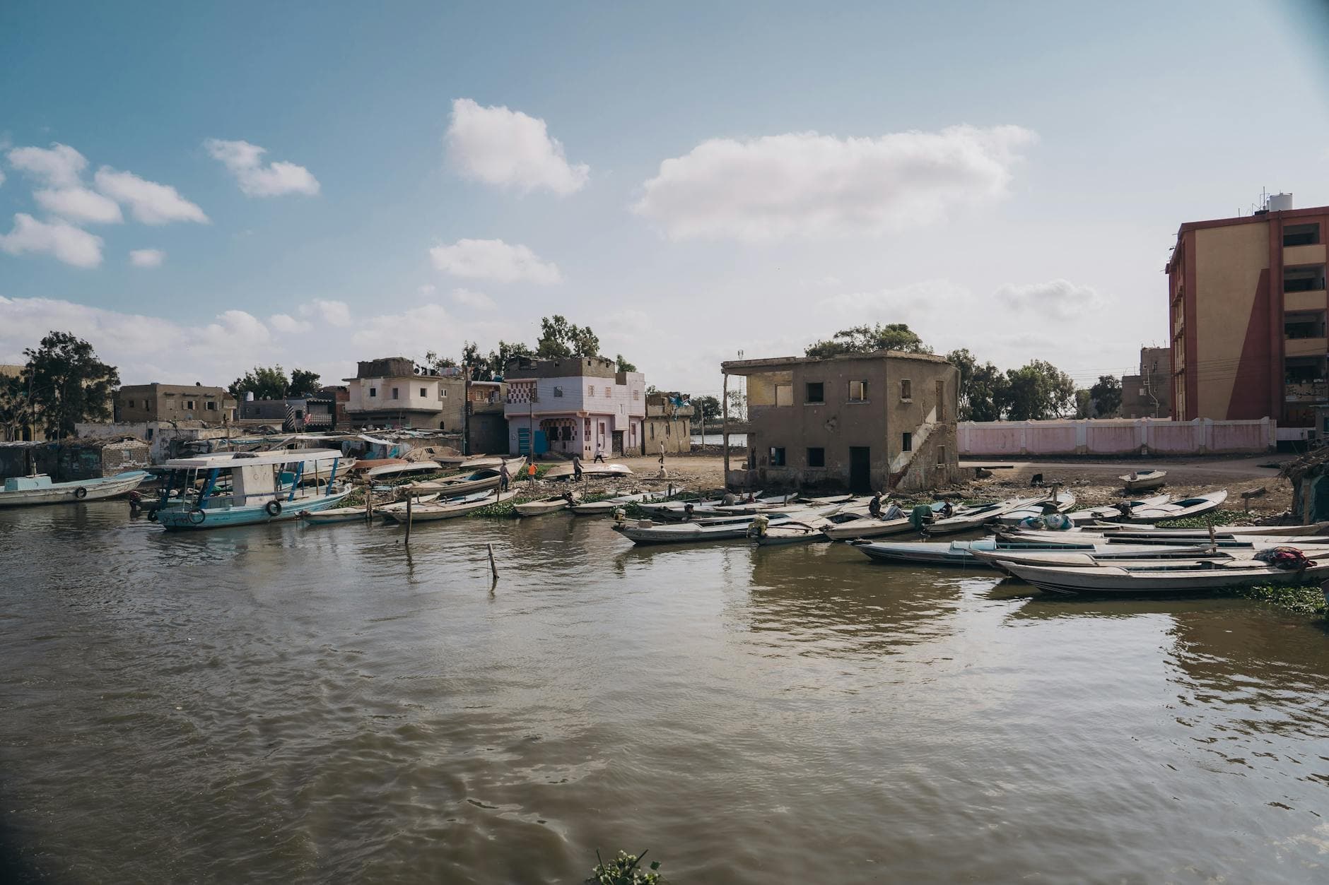 Tranquil waterfront scene in Kafr El-Shaikh, Egypt with boats and historic buildings.