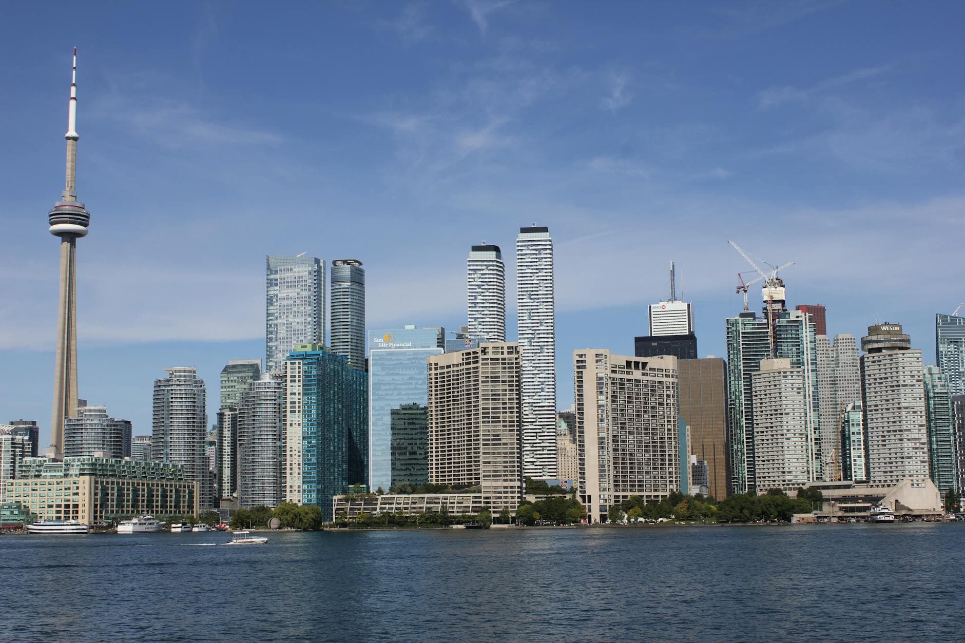 Urban skyline view of Toronto with the iconic CN Tower and waterfront skyscrapers under blue skies.