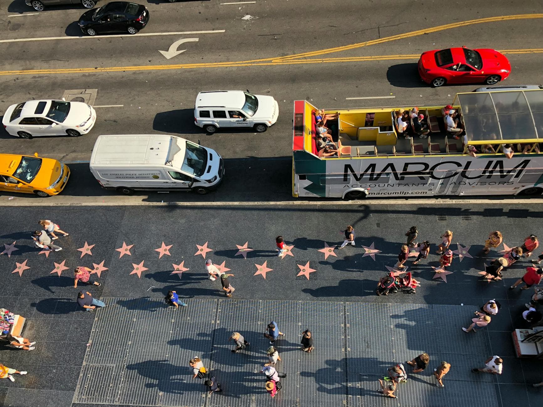 Bird's-eye view of Hollywood Walk of Fame with tourists and vehicles on a sunlit afternoon.