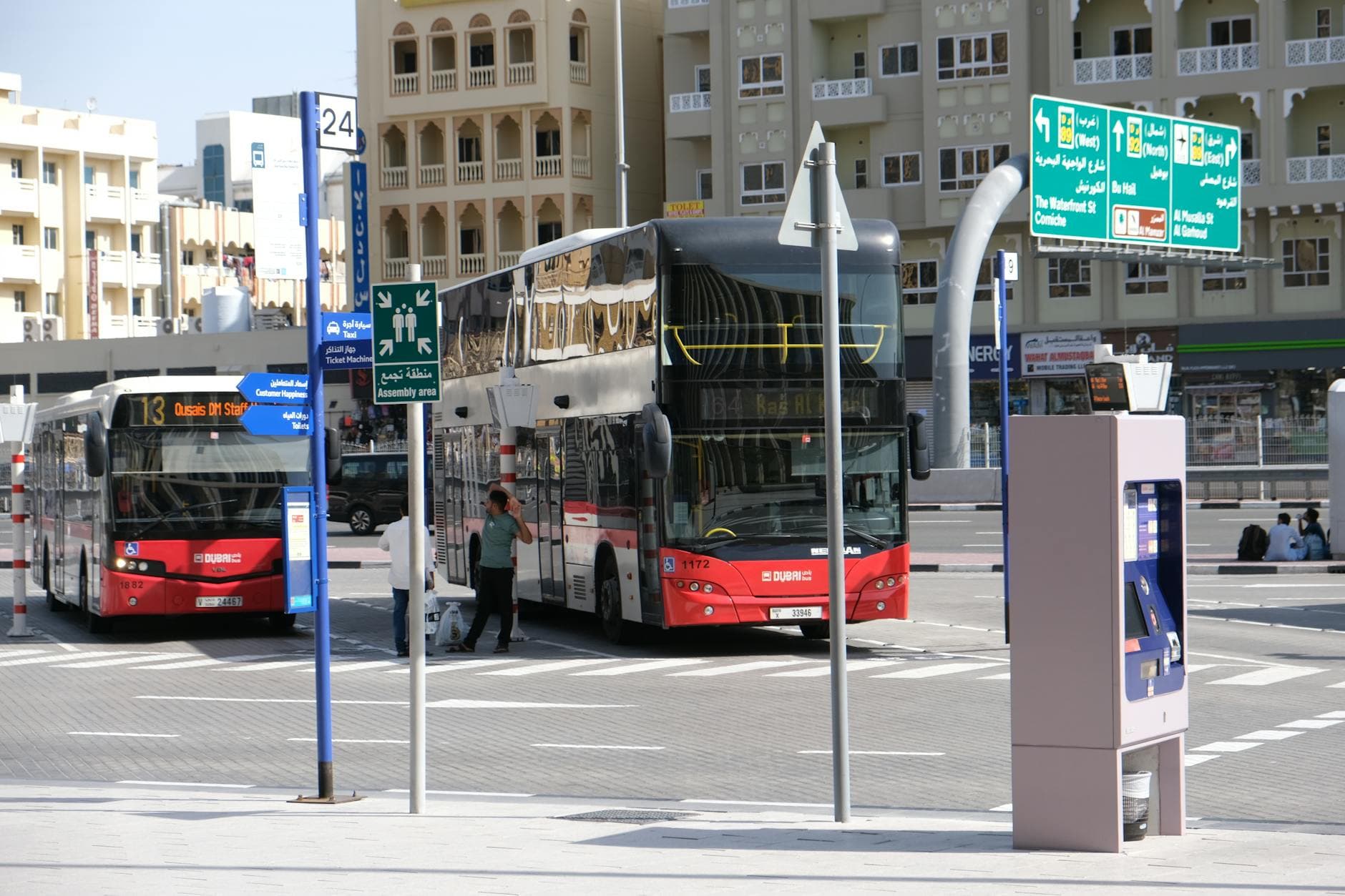 Public bus station in downtown Dubai with red buses and street signs visible.