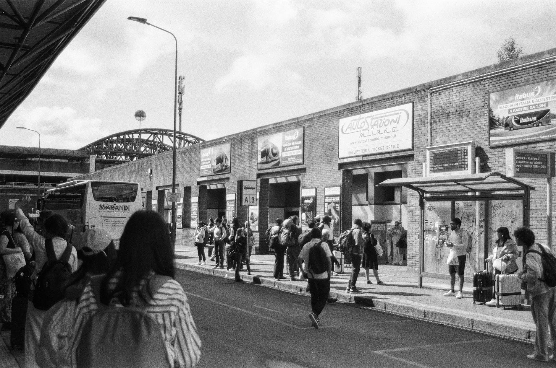 Black and white photo capturing people at a bustling bus station in Milan, Italy.