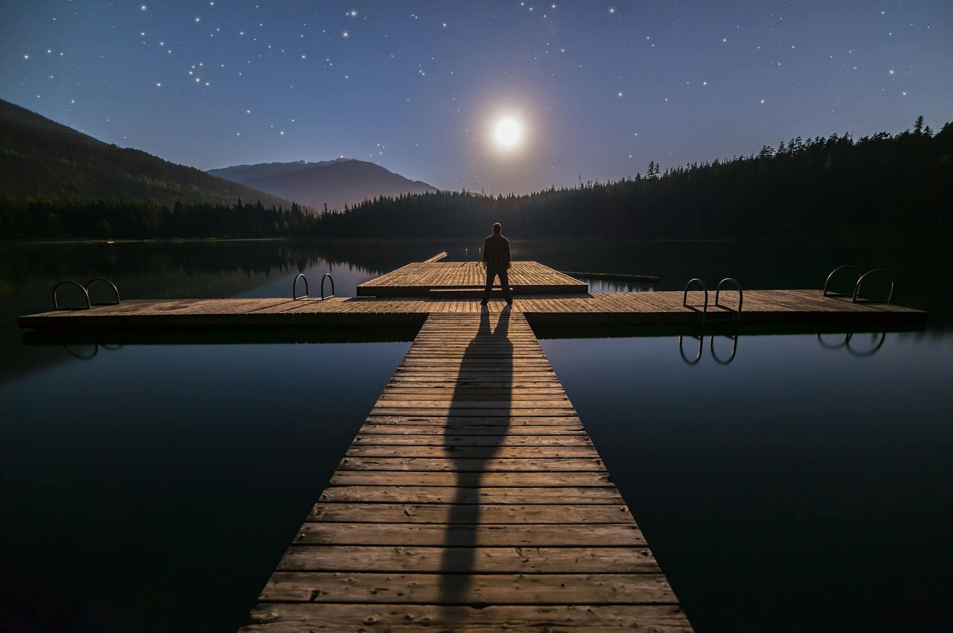 A man stands alone on a dock under a starry night sky in Whistler, BC, Canada.
